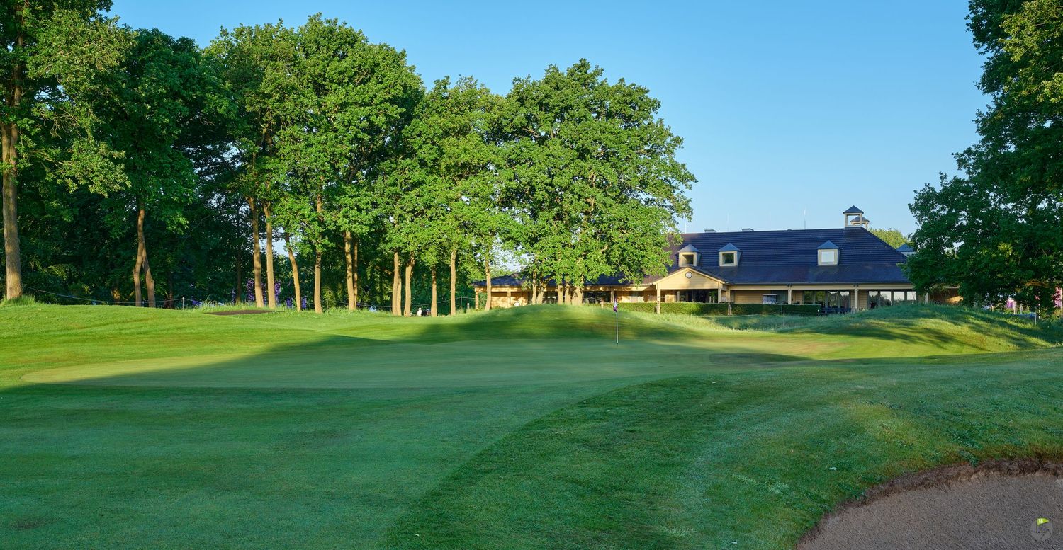 Expansive golf course fairway leading to a clubhouse, framed by mature trees under a bright blue summer sky.