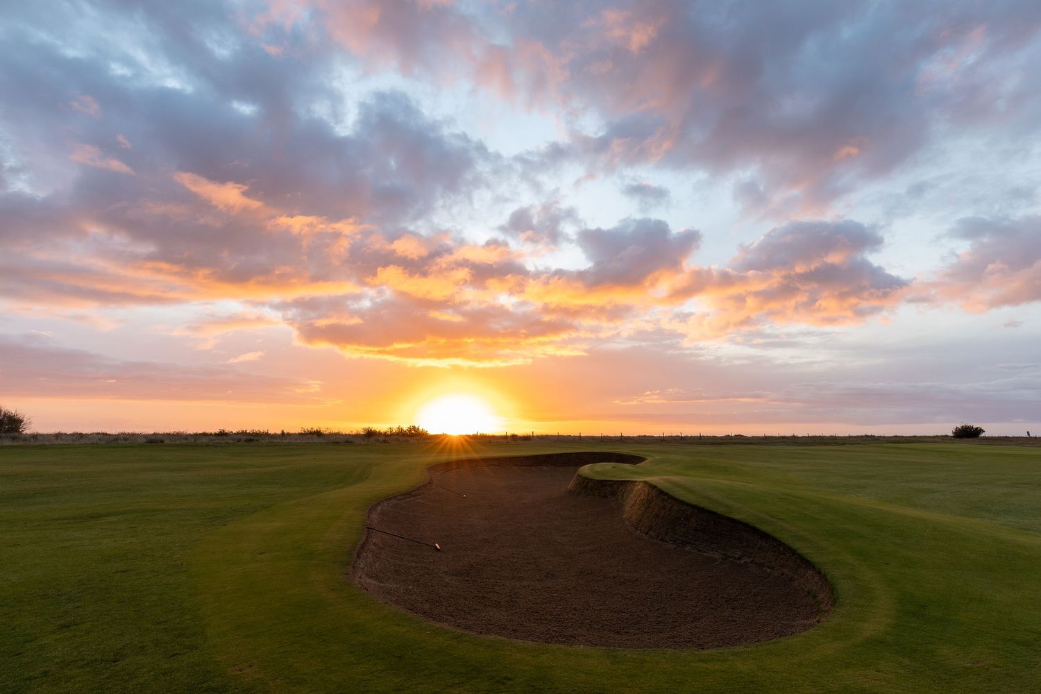 Stunning sunset over a golf course bunker with vibrant pink and orange clouds illuminating the sky.