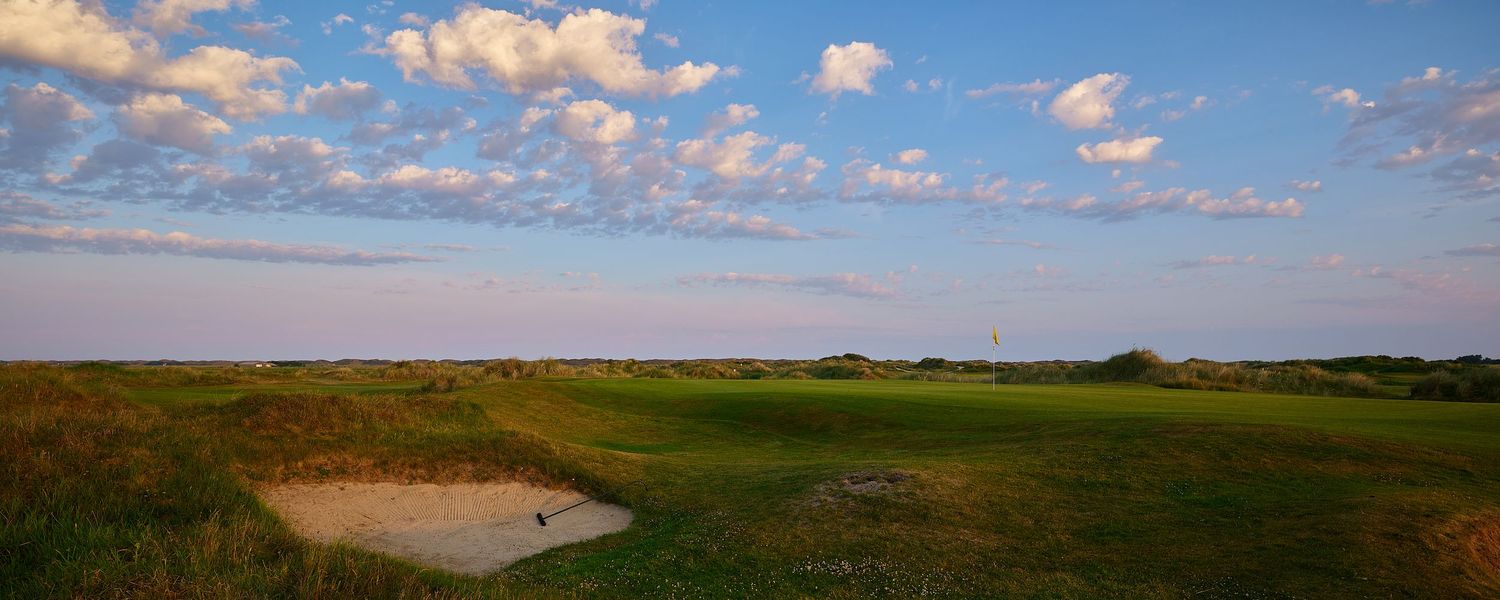 Scenic links golf course fairway with sand bunker under blue sky with fluffy white clouds on a sunny day.