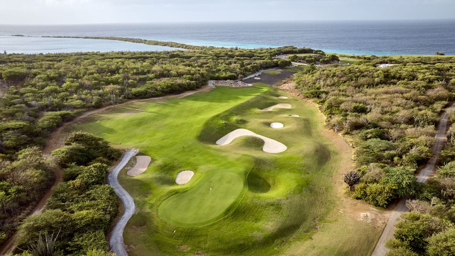 Panoramic view of a coastal golf course with dramatic cliffs, bunkers, and rolling green fairways overlooking the ocean.