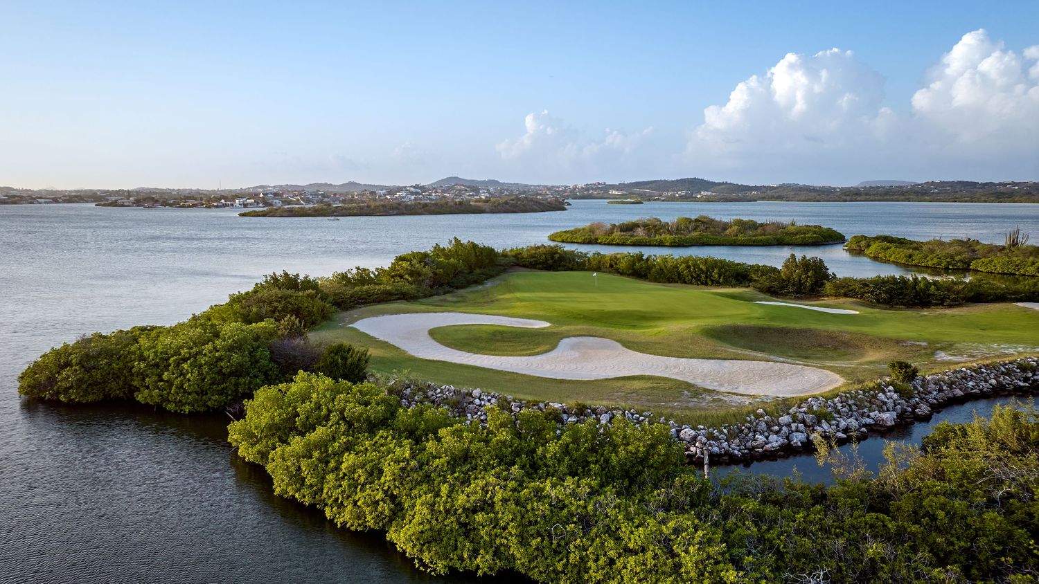 A panoramic coastal landscape shows golf courses, waterways, and lush mangroves under a bright blue sky.