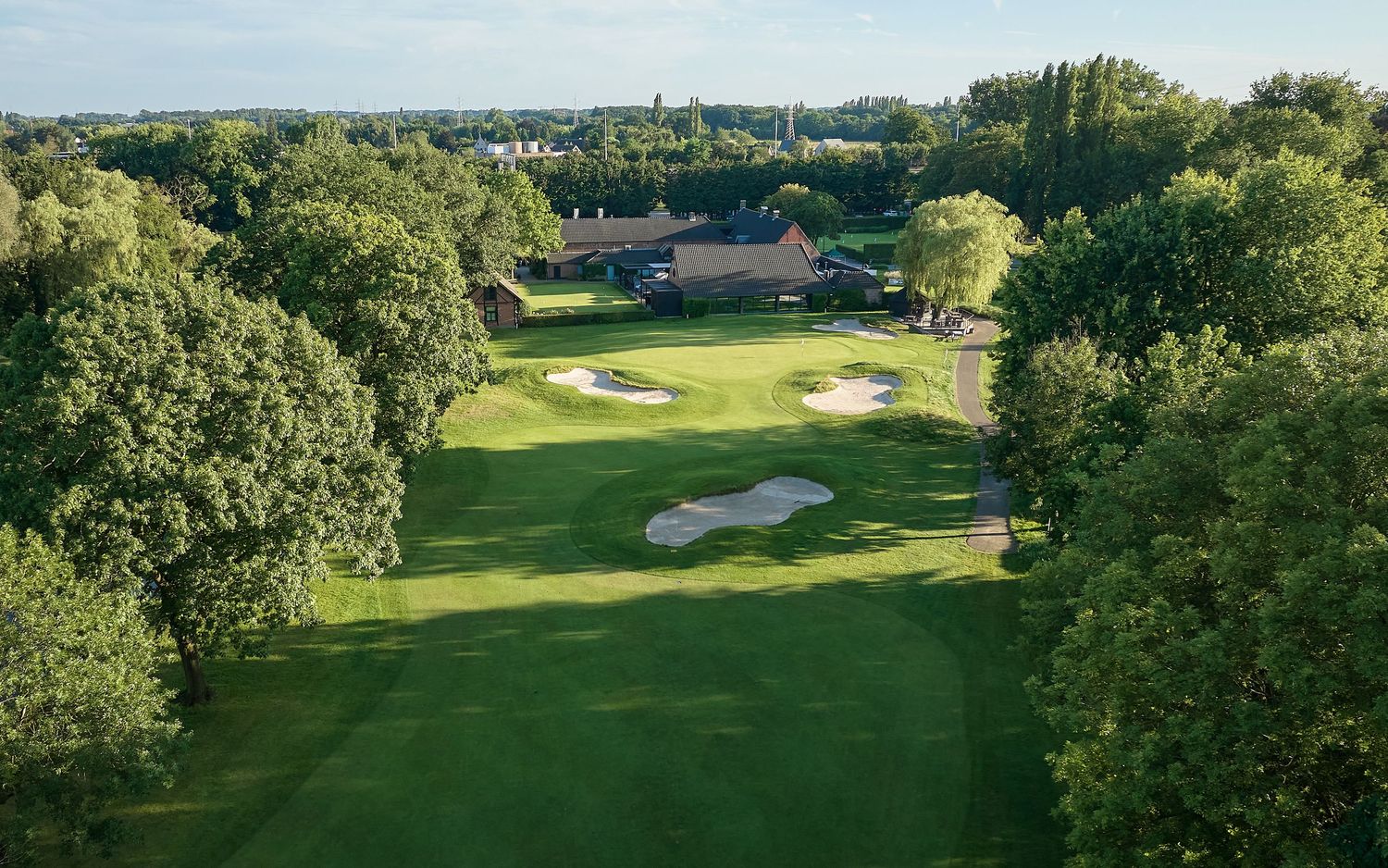 Aerial view of a lush green golf course with sand bunkers, surrounded by mature trees and a clubhouse.
