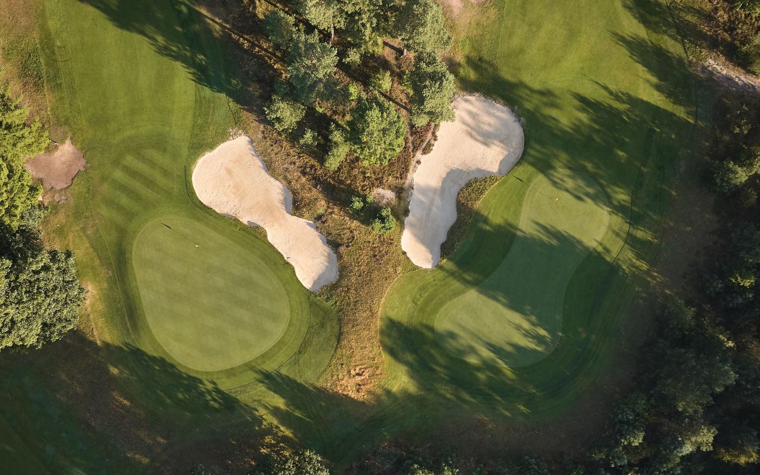 Overhead drone shot of pristine golf course greens with strategically placed sand traps and manicured fairways.