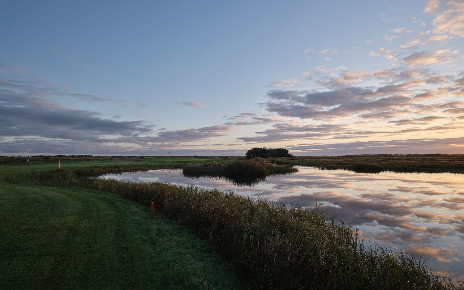 A panoramic view of a serene coastal landscape with dramatic clouds reflecting in still waters at sunset.