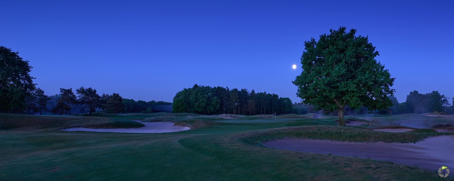 Twilight panoramic view of a serene golf course with sand bunkers and a full moon rising.