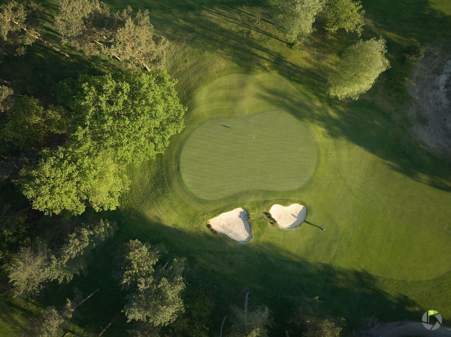 Aerial view of a lush green golf course hole with two sand bunkers surrounded by trees.