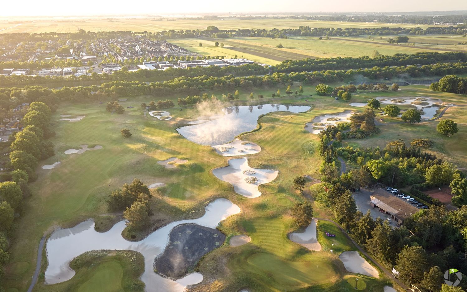 Aerial view of a scenic golf course with sand bunkers, water features, and lush fairways at golden hour.