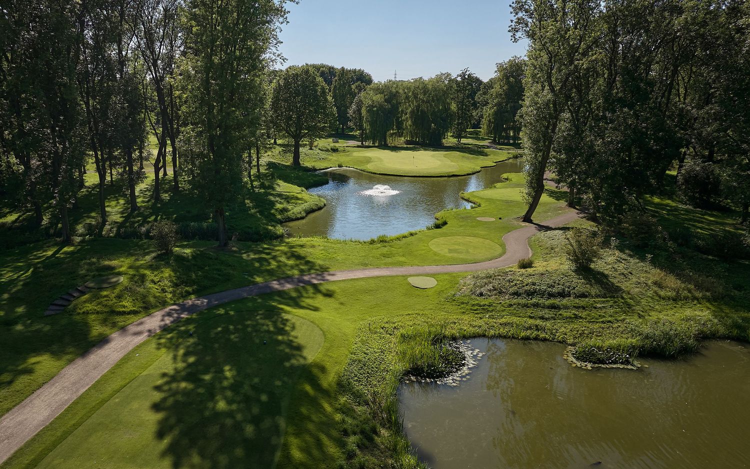 Aerial view of a lush golf course with water features, fountains, and tree-lined fairways on a sunny day.