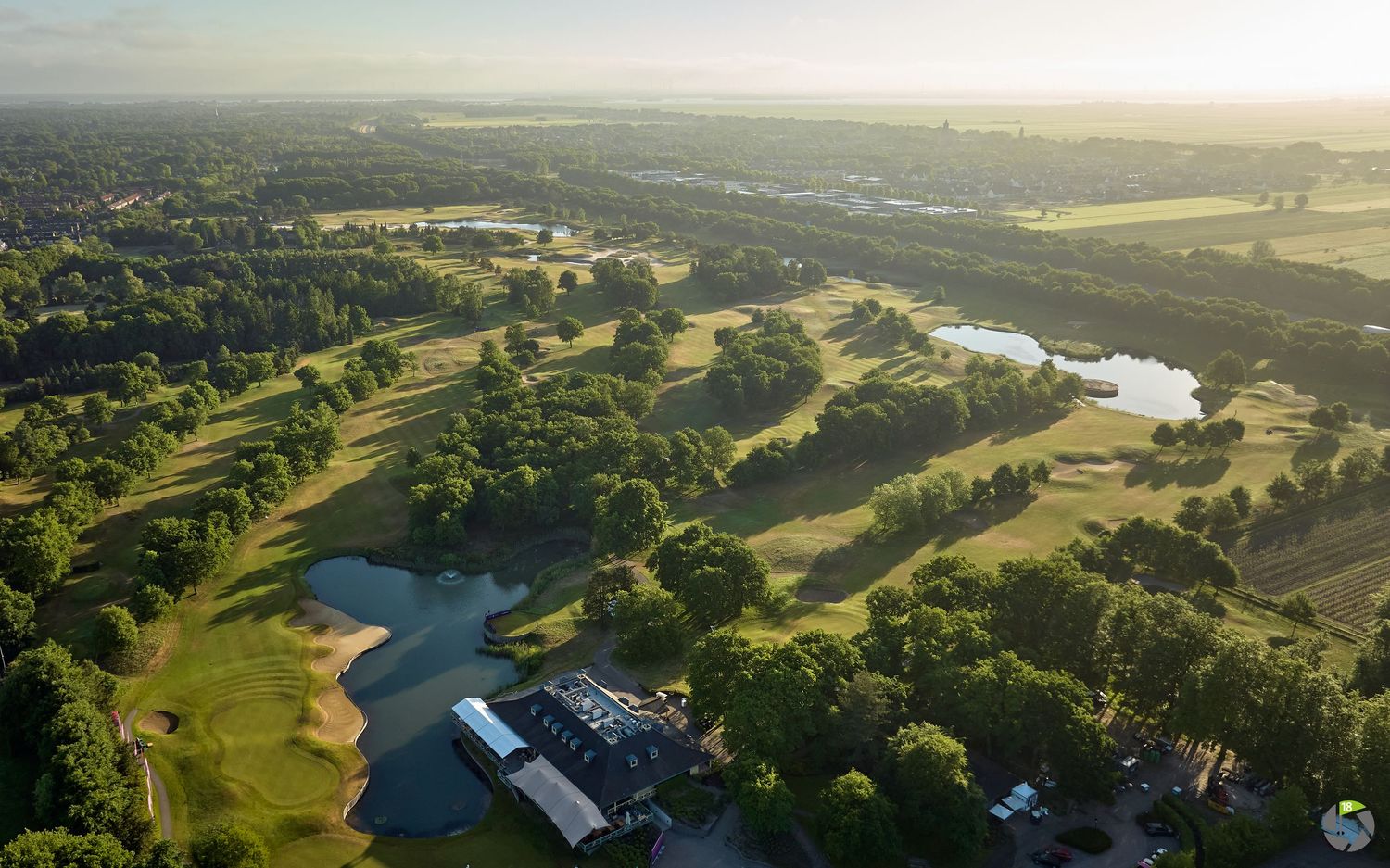 Aerial view of a lush golf course with lakes, trees, and a clubhouse in the countryside.