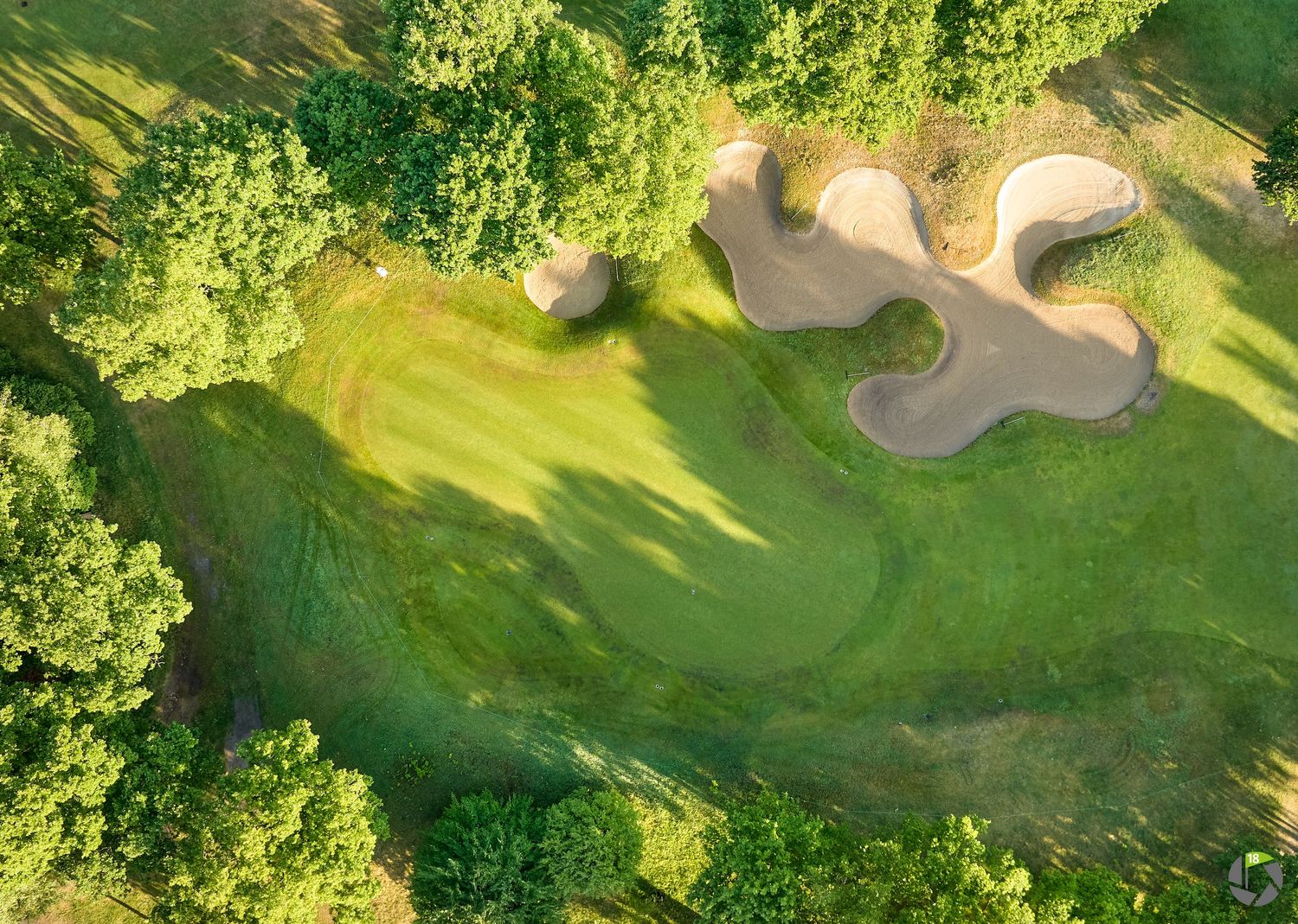 Aerial view of a lush green golf course fairway surrounded by trees with sand bunkers near the putting green.