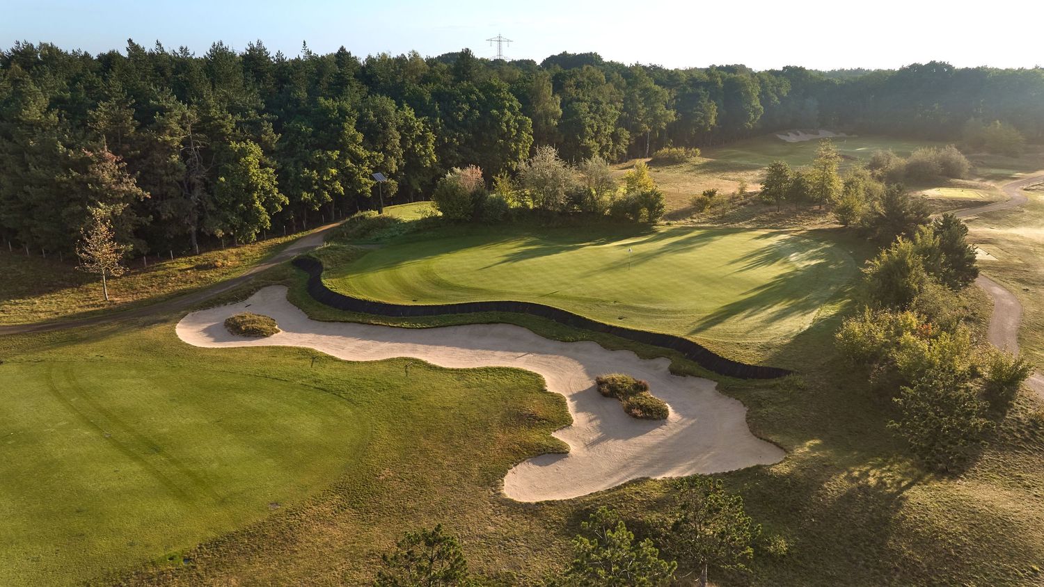 Elevated view of a golf hole with large sand bunkers and dense tree line backdrop.