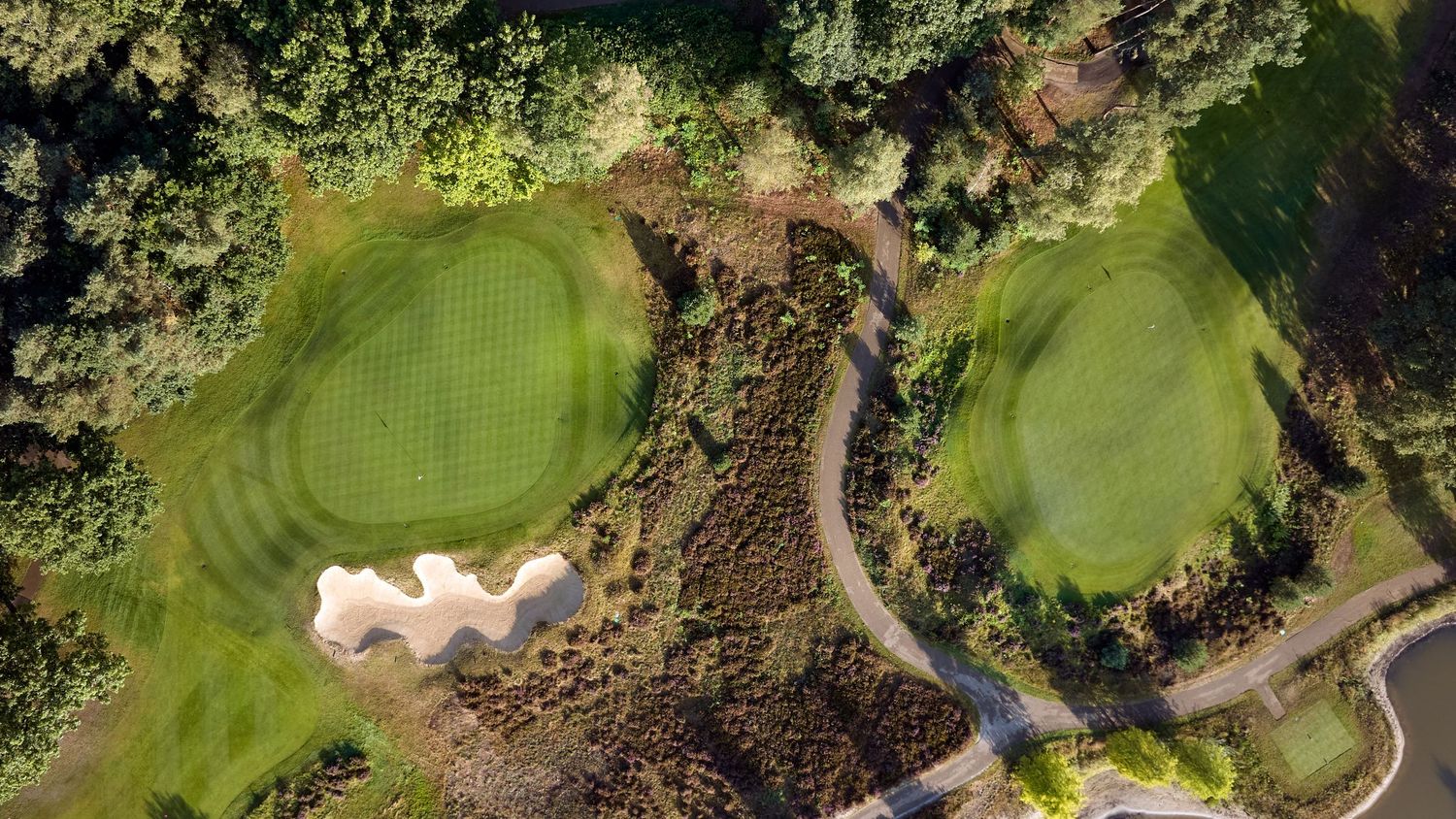 Aerial view of a golf course showing two greens, sand bunkers, and surrounding woodland.