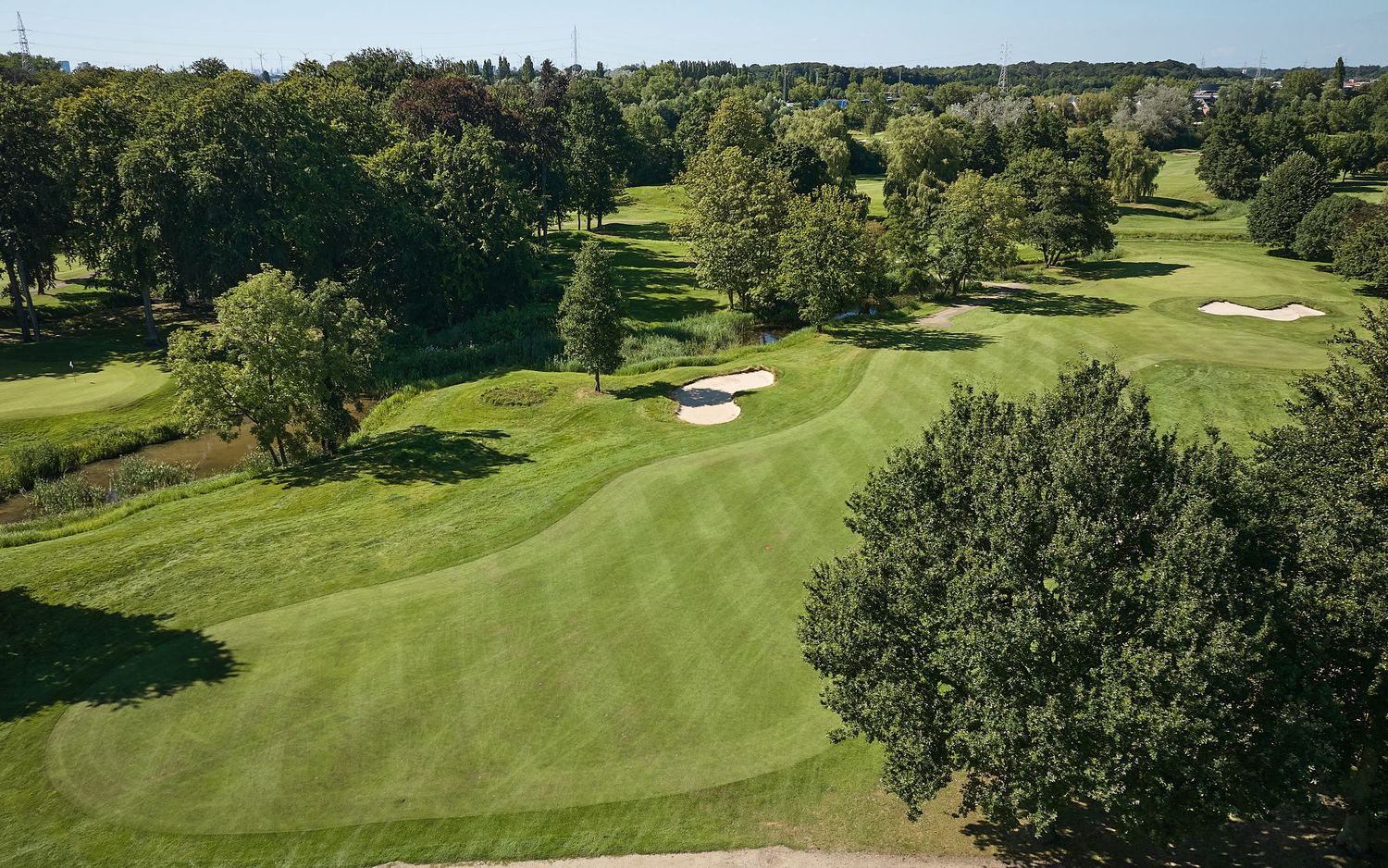 Aerial view of a lush green golf course fairway with sand bunkers surrounded by mature trees.