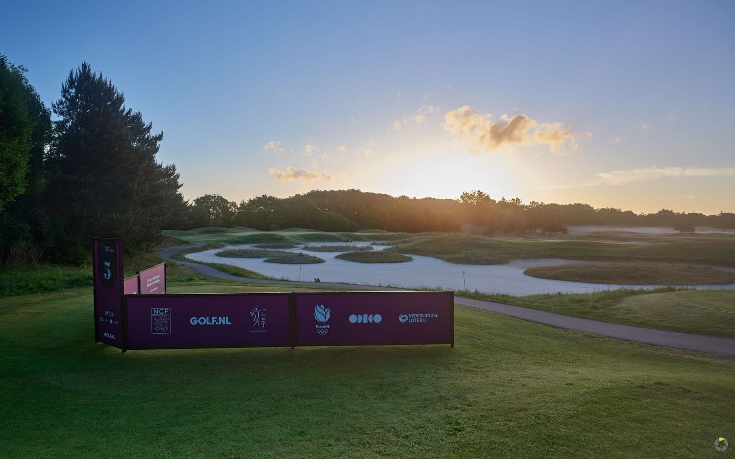 Stunning sunset over a golf course water hazard with tournament signage and lush green fairways.