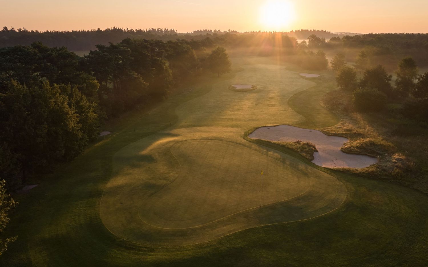 Sunset panorama over rolling golf course terrain with dramatic shadows across greens and water hazards.