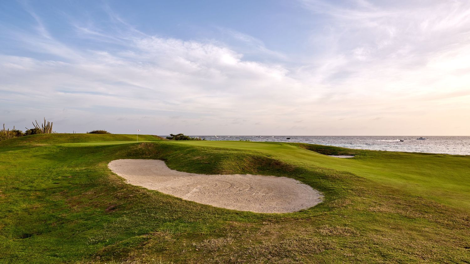Scenic coastal golf course with sand bunker overlooking the ocean during sunset.