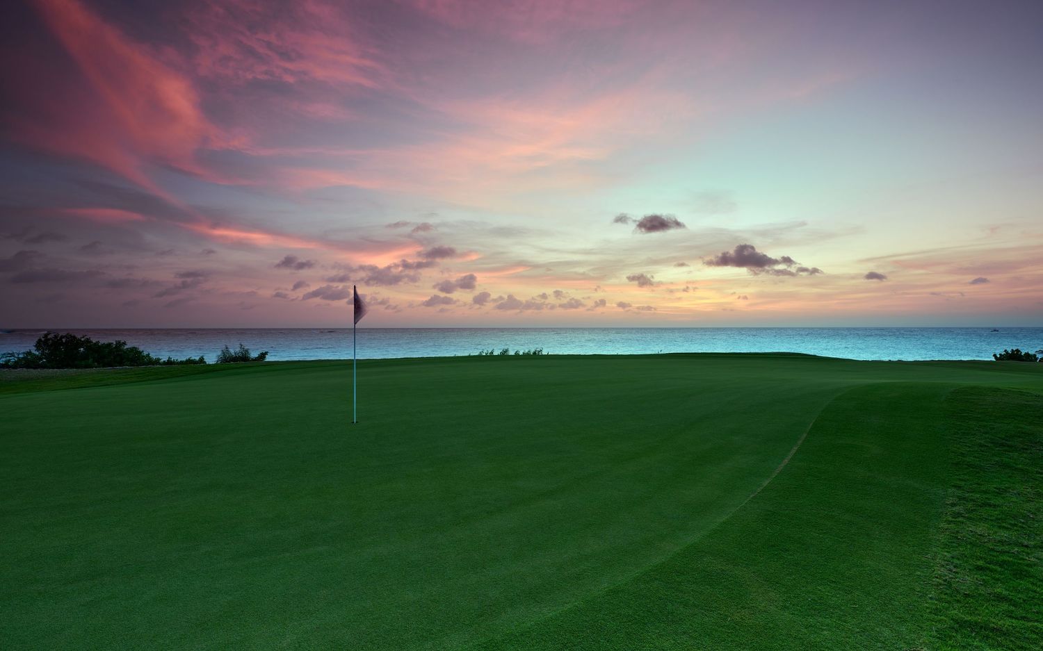 A stunning panoramic view of a golf course with rolling green hills against a vibrant sunset sky.