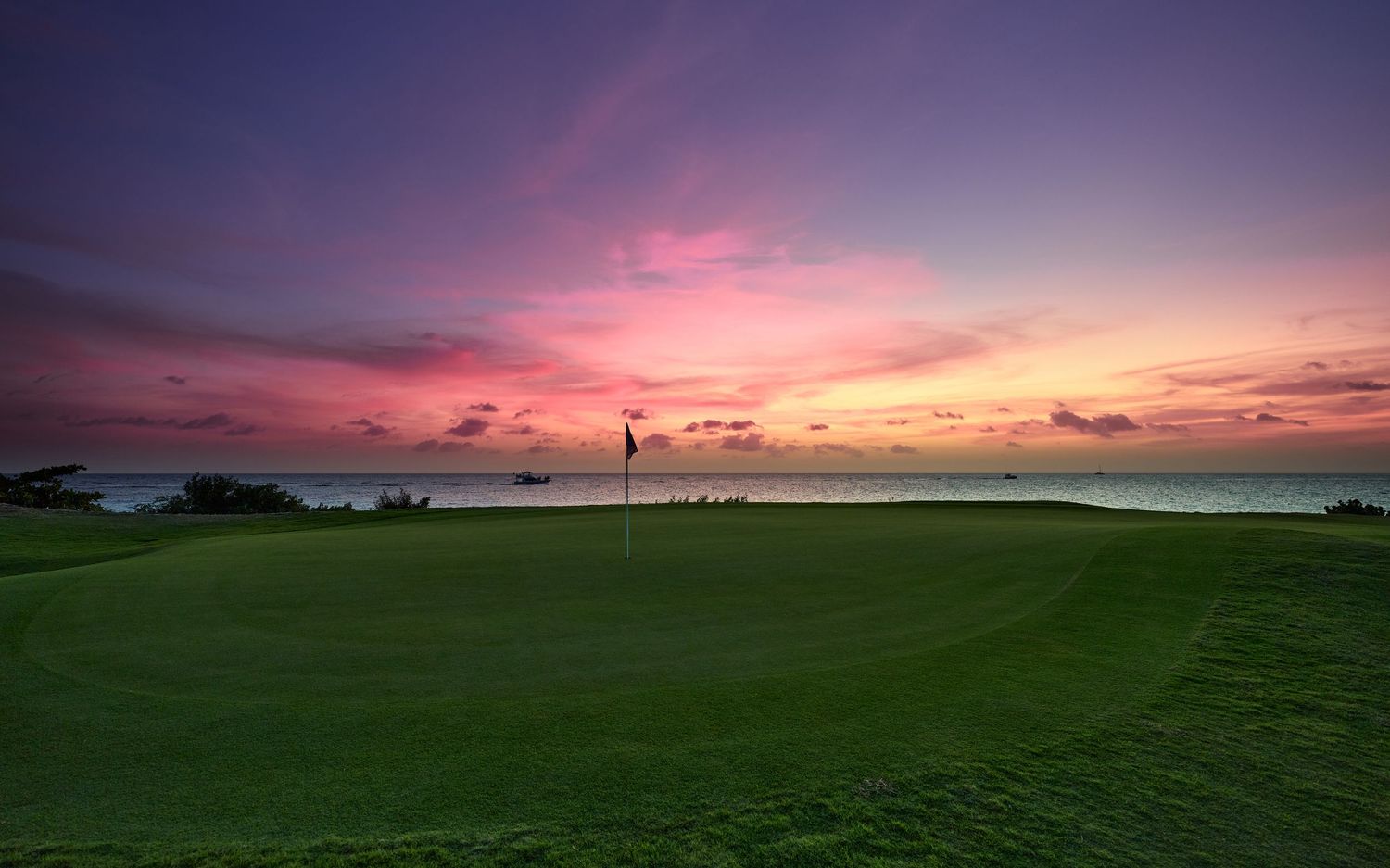 Stunning panoramic view of a vibrant sunset over a coastal golf course with dramatic pink and orange clouds.