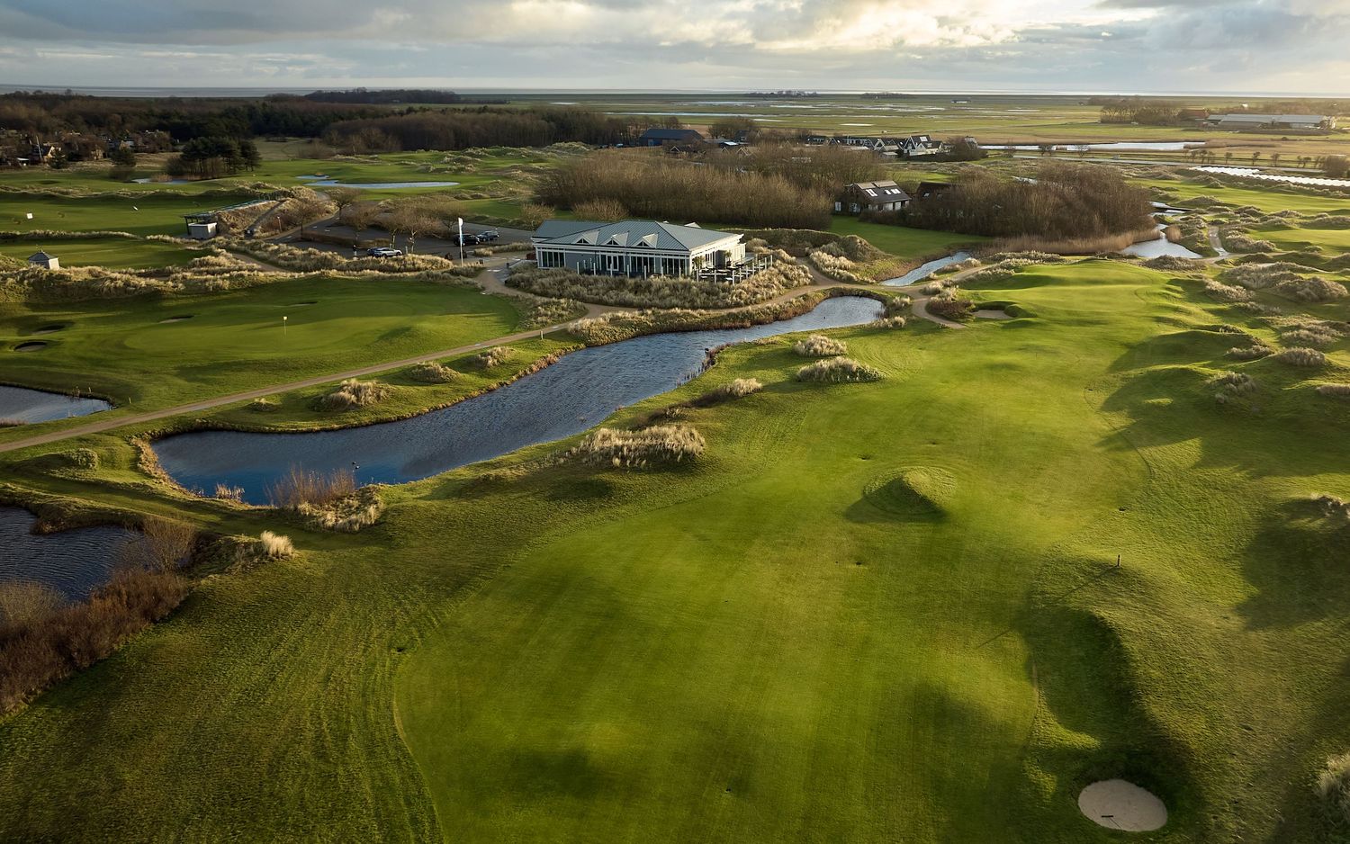 Aerial view of a lush green golf course with water hazards and a clubhouse under a cloudy sky.