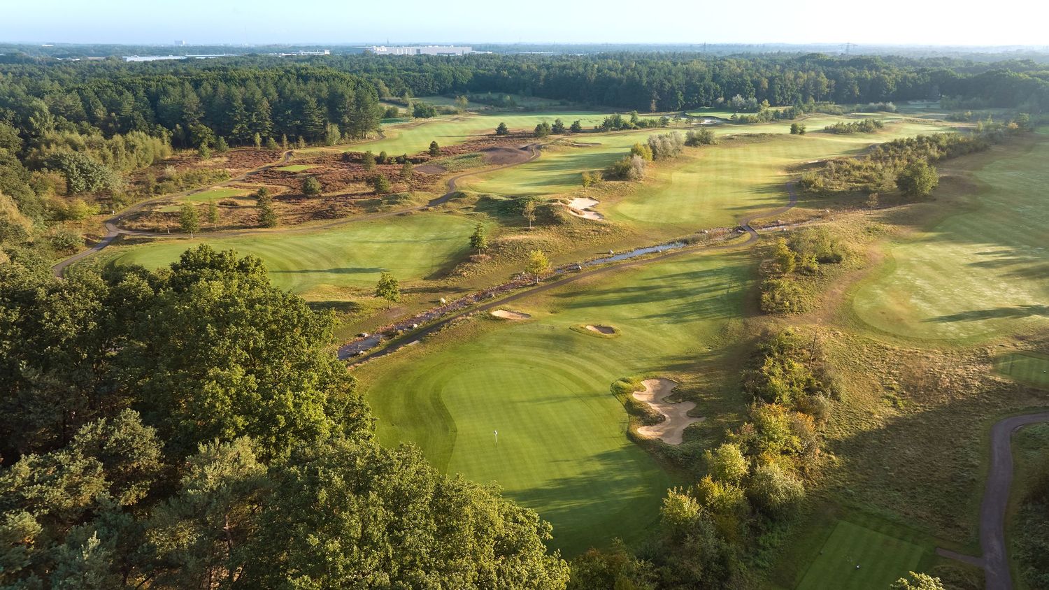 Aerial view of a sprawling golf course with fairways, bunkers, and dense forest in autumn.