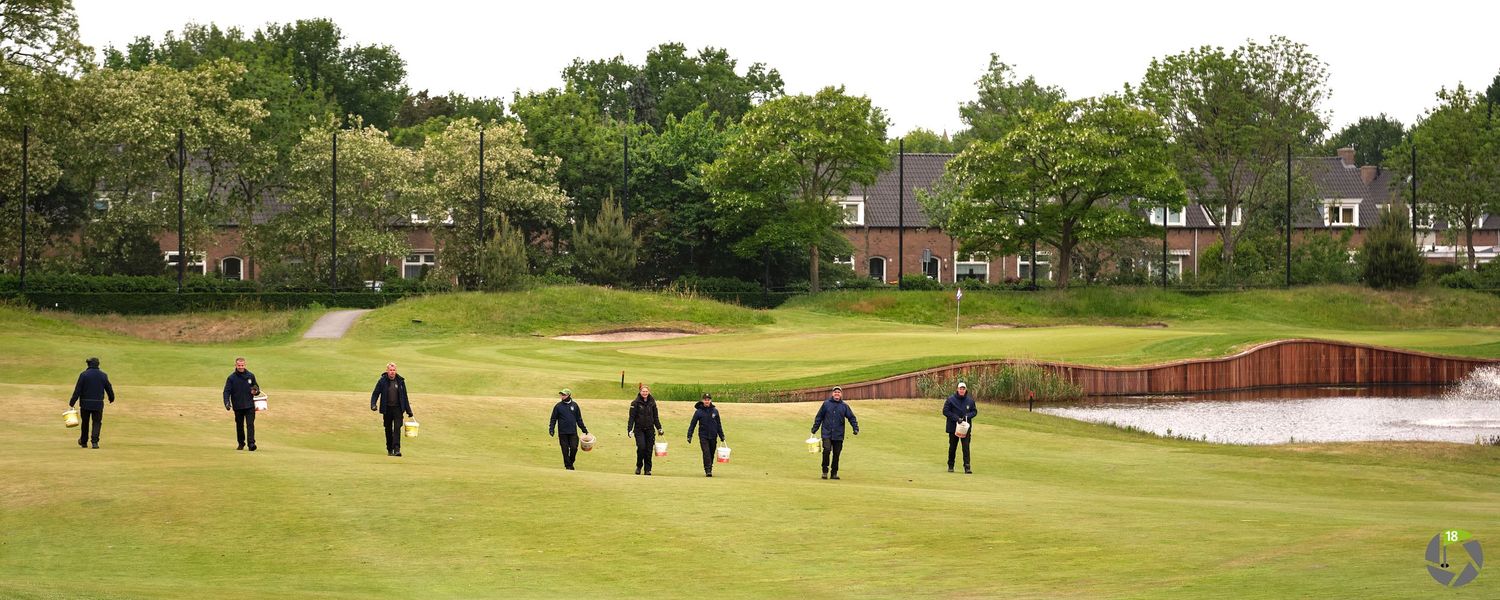 Golfers walking across a lush green fairway on a golf course surrounded by trees and residential buildings.