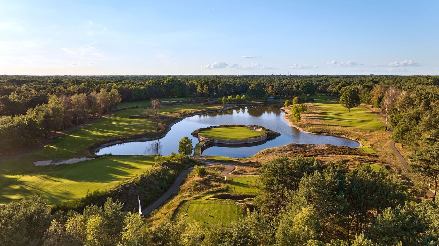 Aerial view of a scenic golf course with winding water hazards and lush green fairways surrounded by autumn trees.