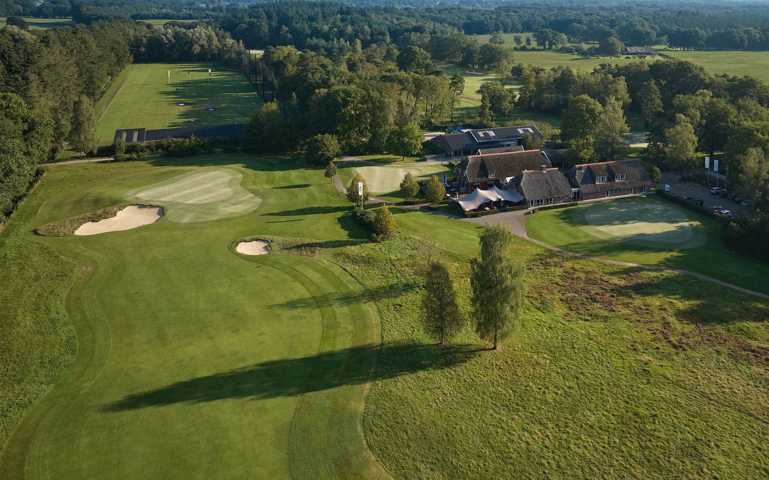 Aerial view of a scenic golf course with lush fairways, sand bunkers and tree-lined holes during golden hour.