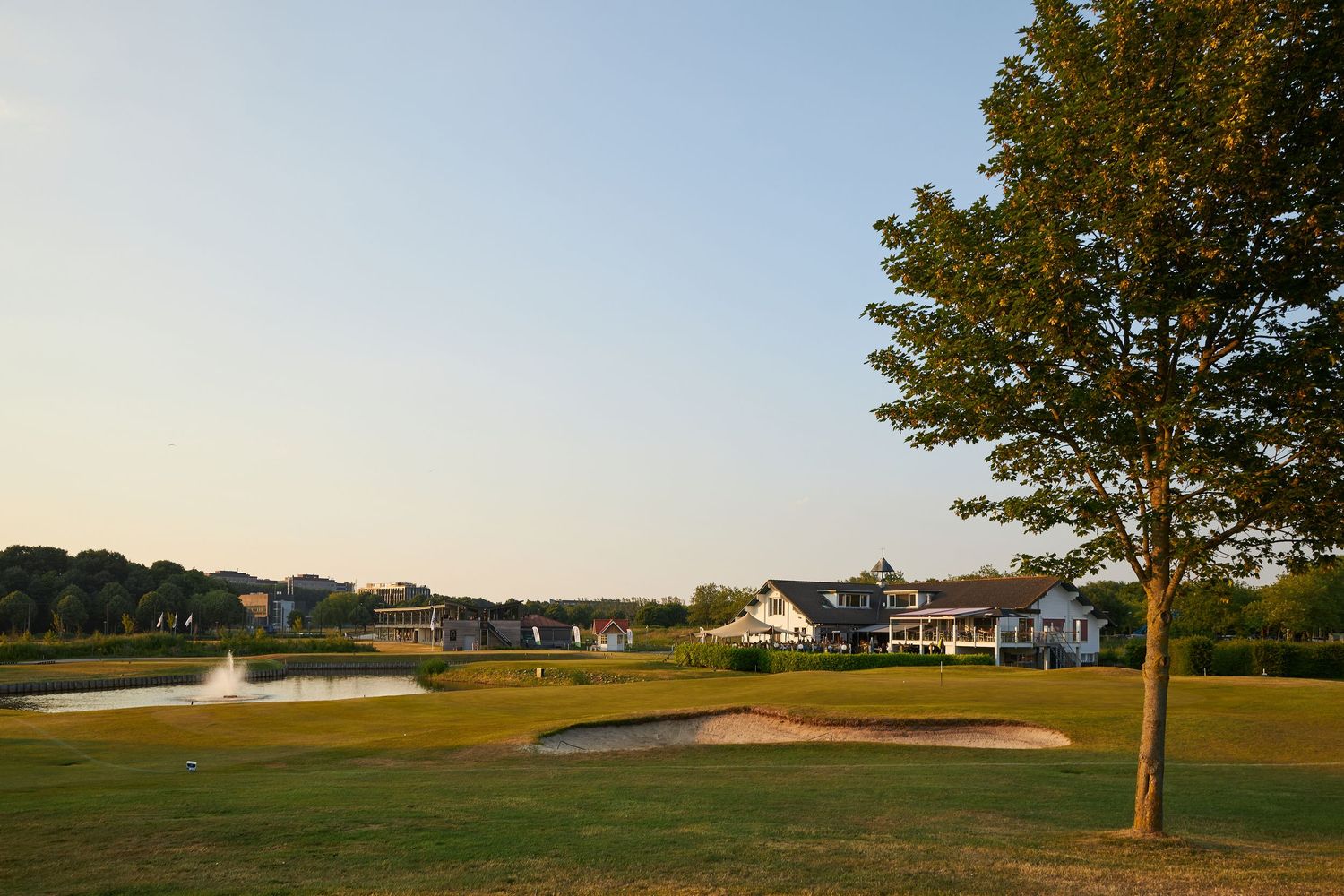 Panoramic view of a scenic golf course with rolling greens, sand bunkers, and trees under a bright blue sky.