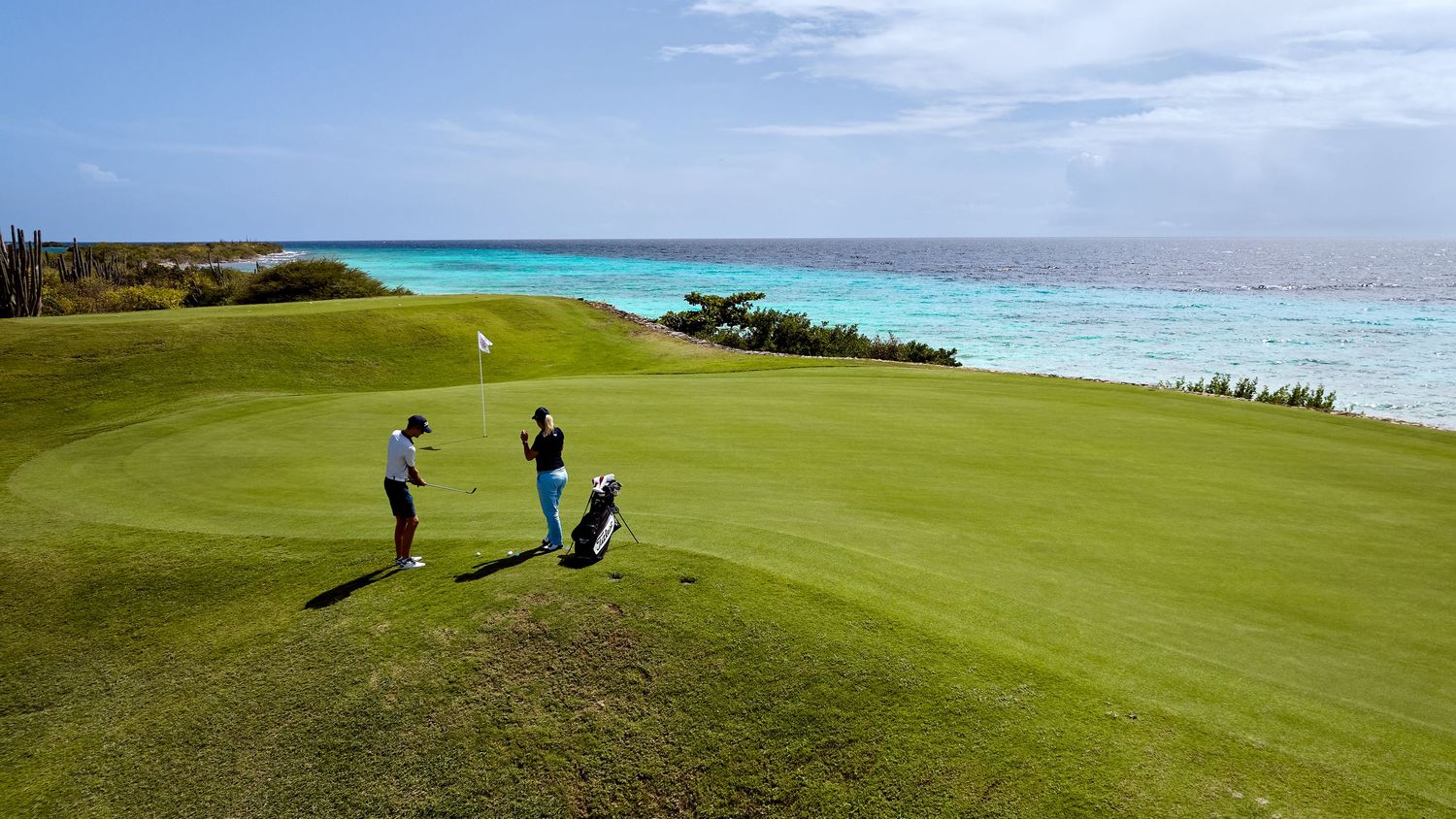 Panoramic view of a coastal golf course with rolling green fairways and blue ocean waters in the background.