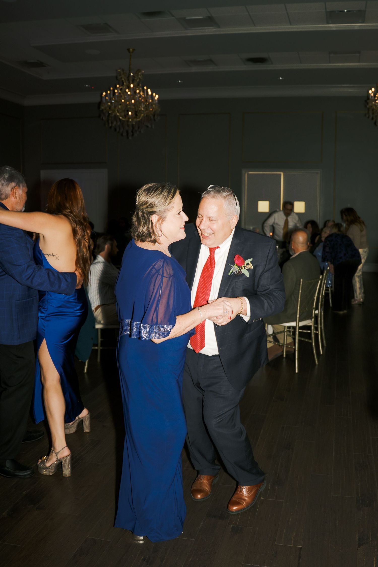 Couples dancing together during an evening wedding reception with chandeliers overhead.