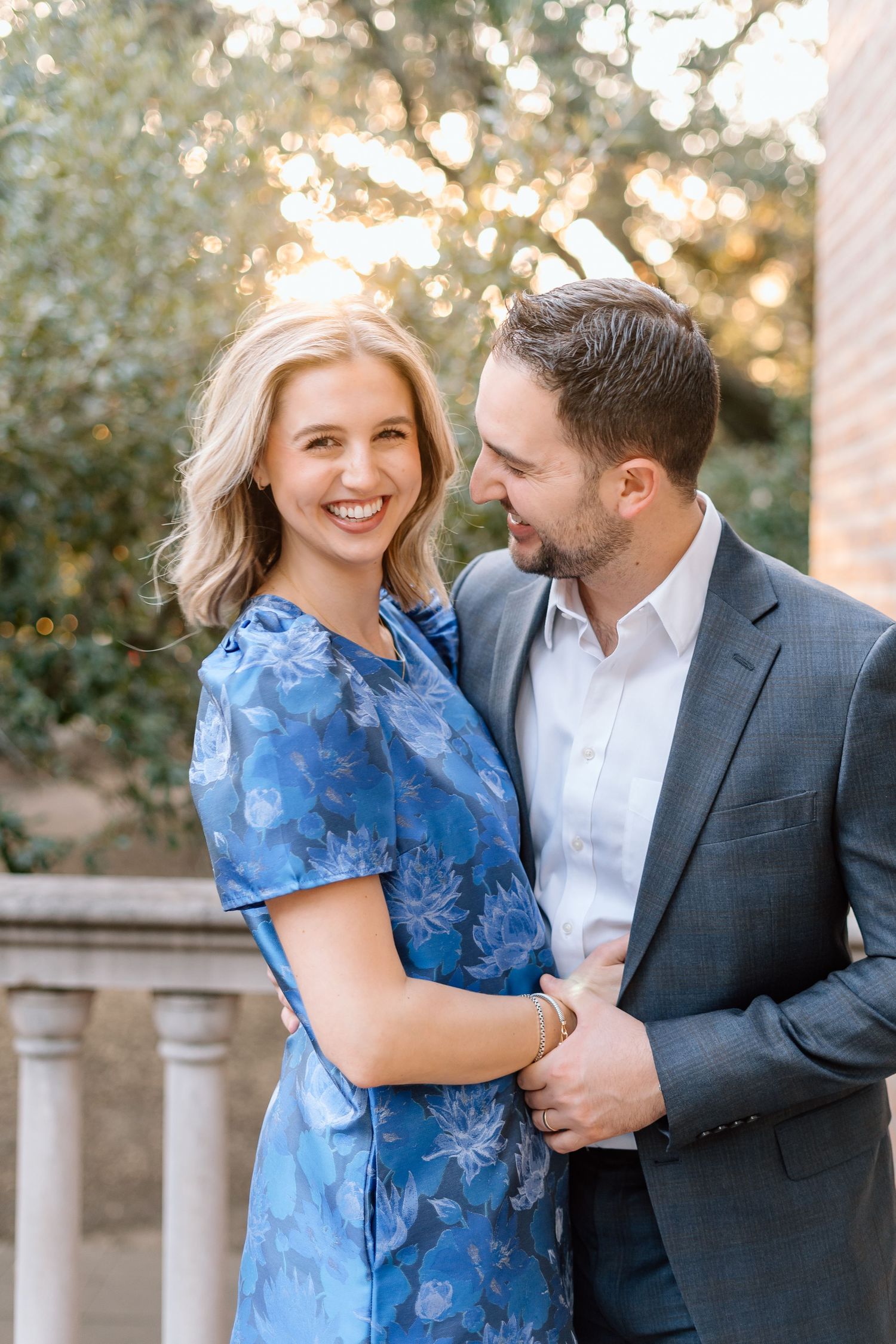 A couple shares a romantic moment outdoors wearing blue and grey formal attire.
