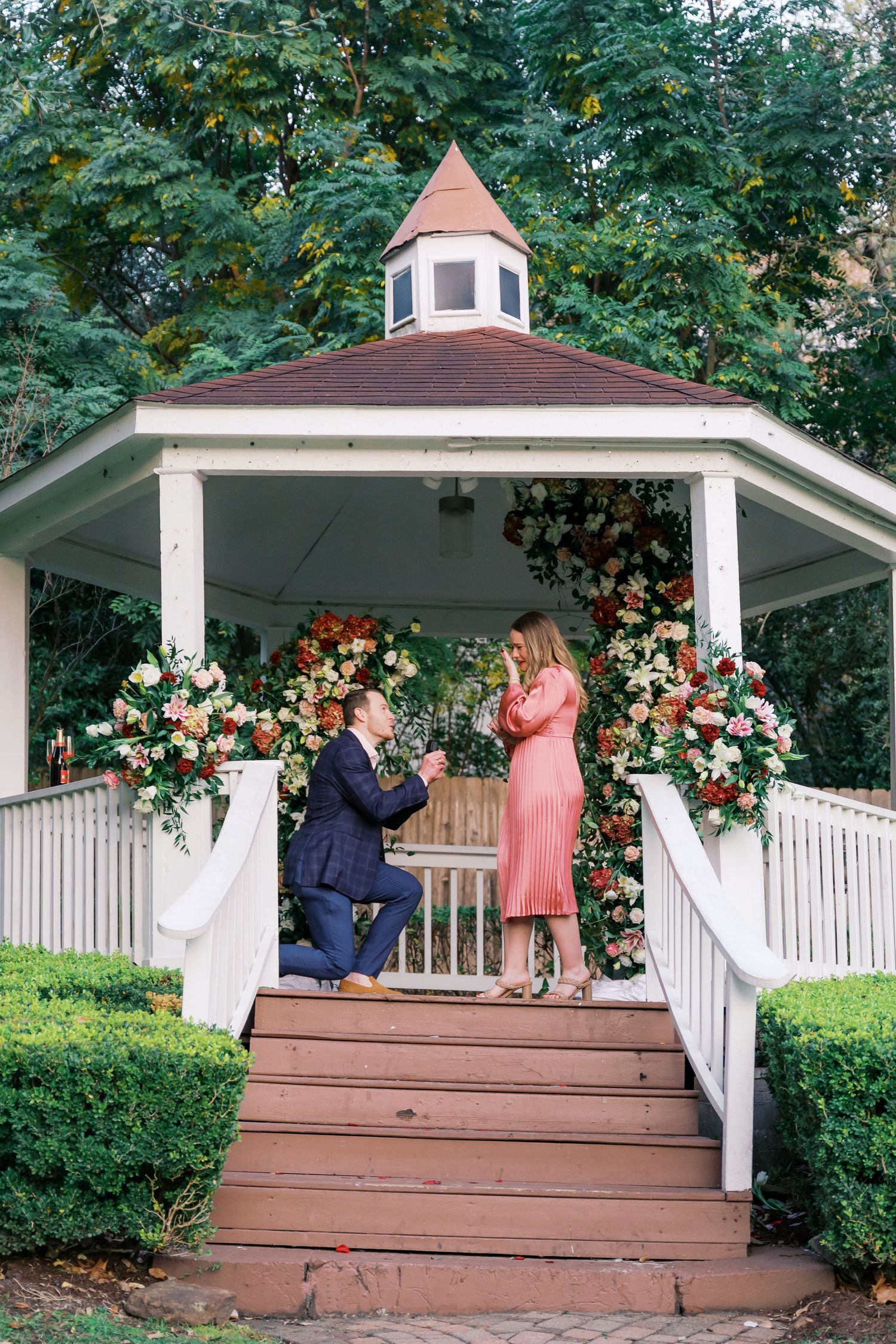 A special moment unfolds on a wooden gazebo deck adorned with pink and white floral arrangements.