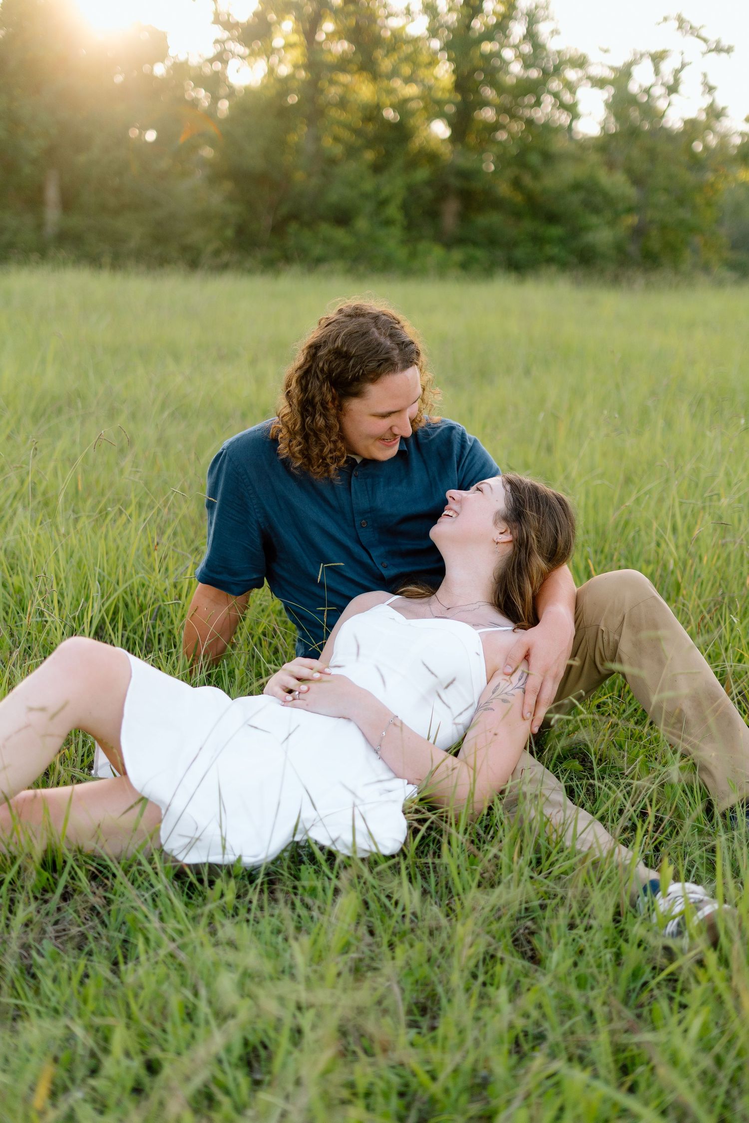 Romantic couple lying together in tall grass during sunset in a field.