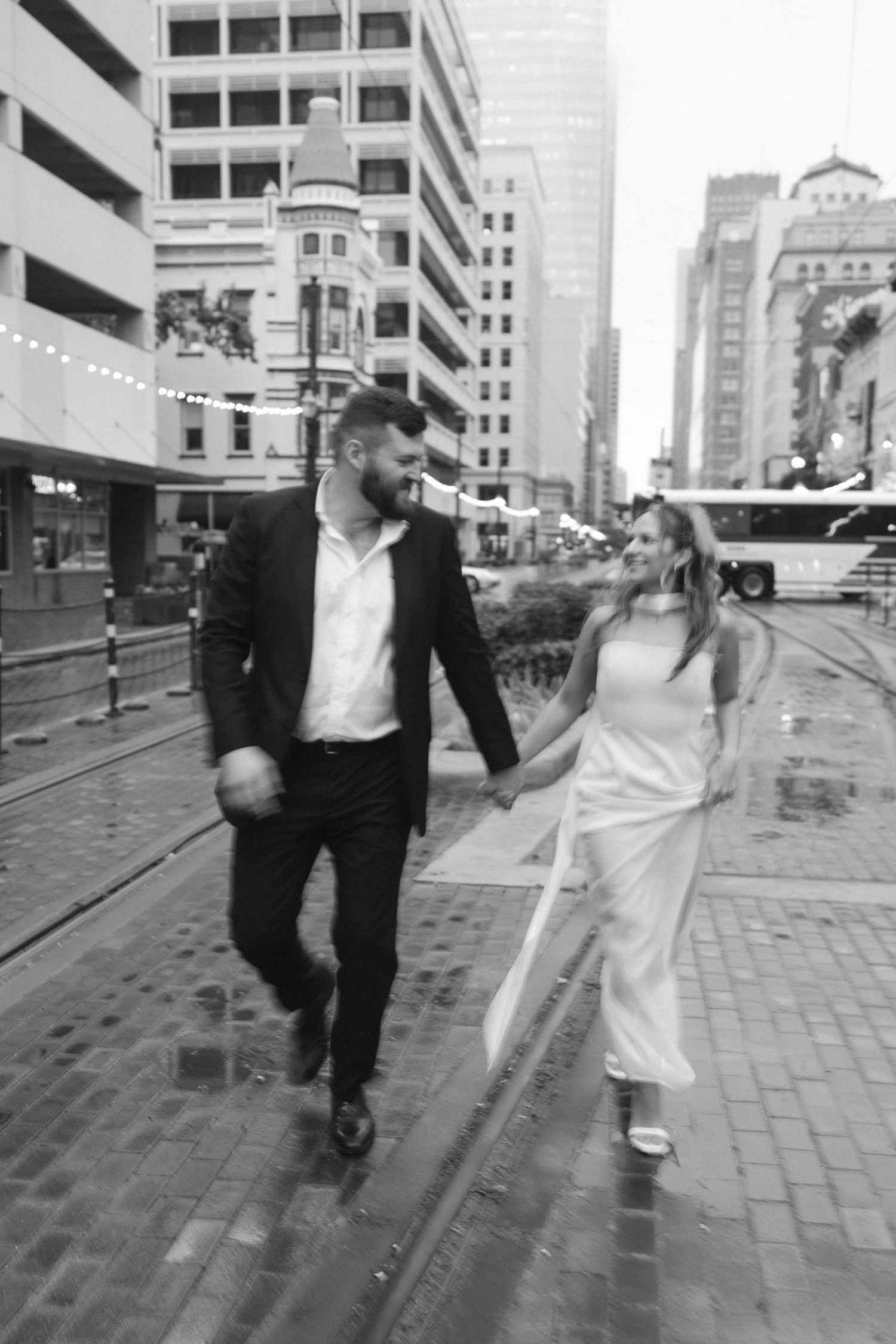 Playful couple dances in the rain on city street with trolley tracks.