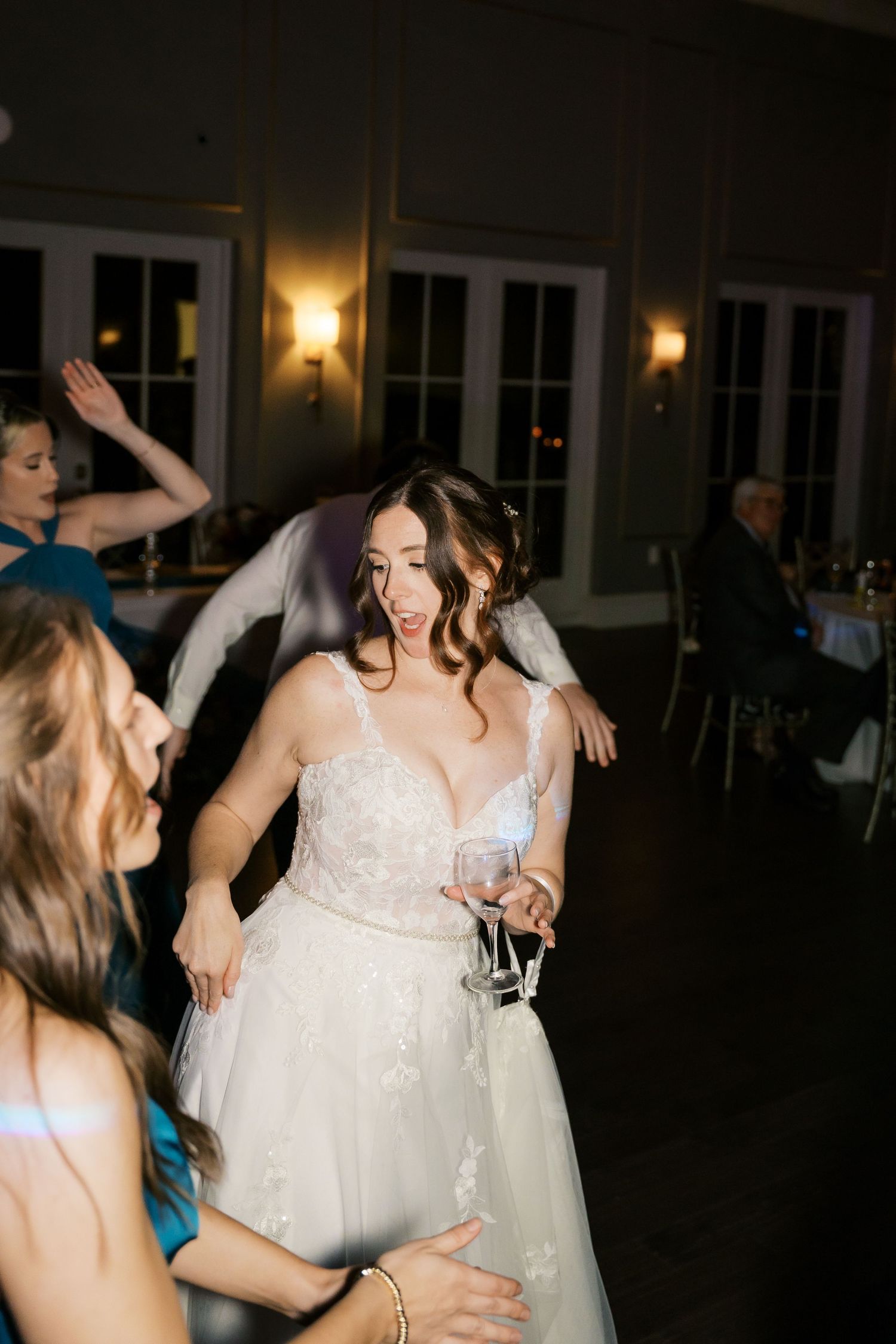 A bride in a white wedding gown dances joyfully at her reception under crystal chandeliers.