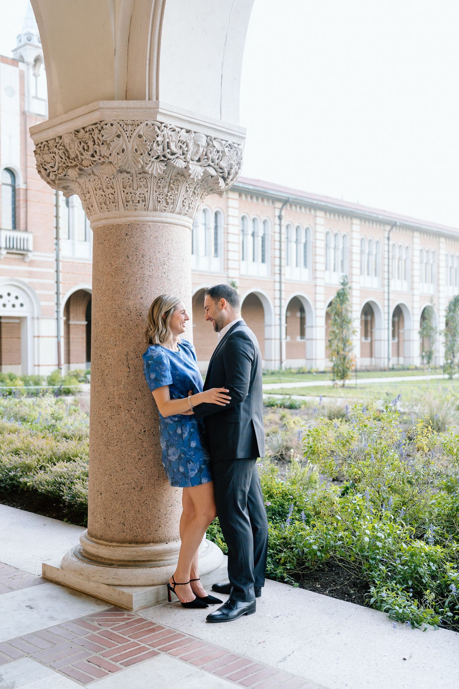 A couple poses playfully under classical architecture with white columns and arches.