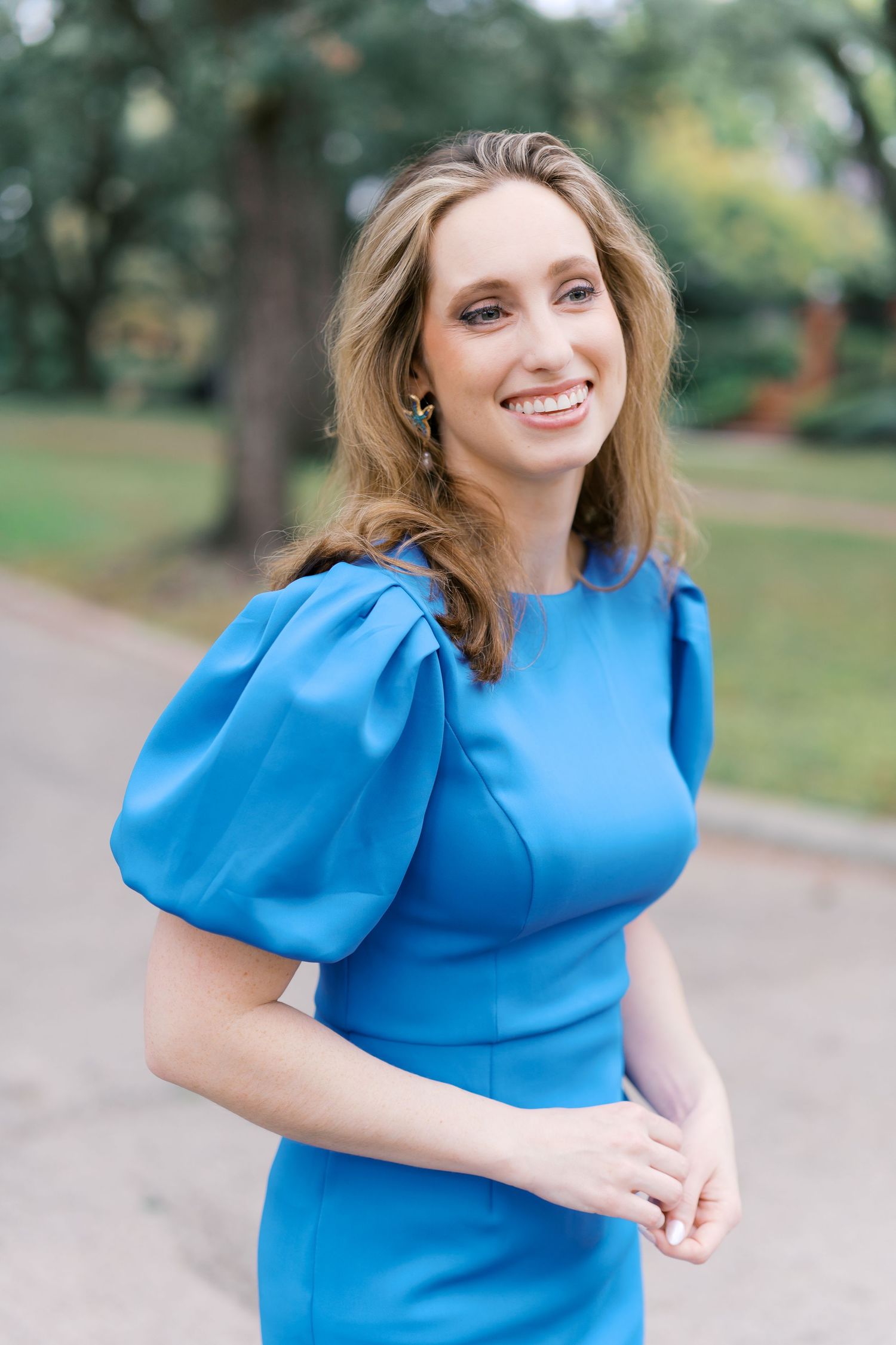 Cheerful outdoor portrait series in vibrant blue dress among park trees.
