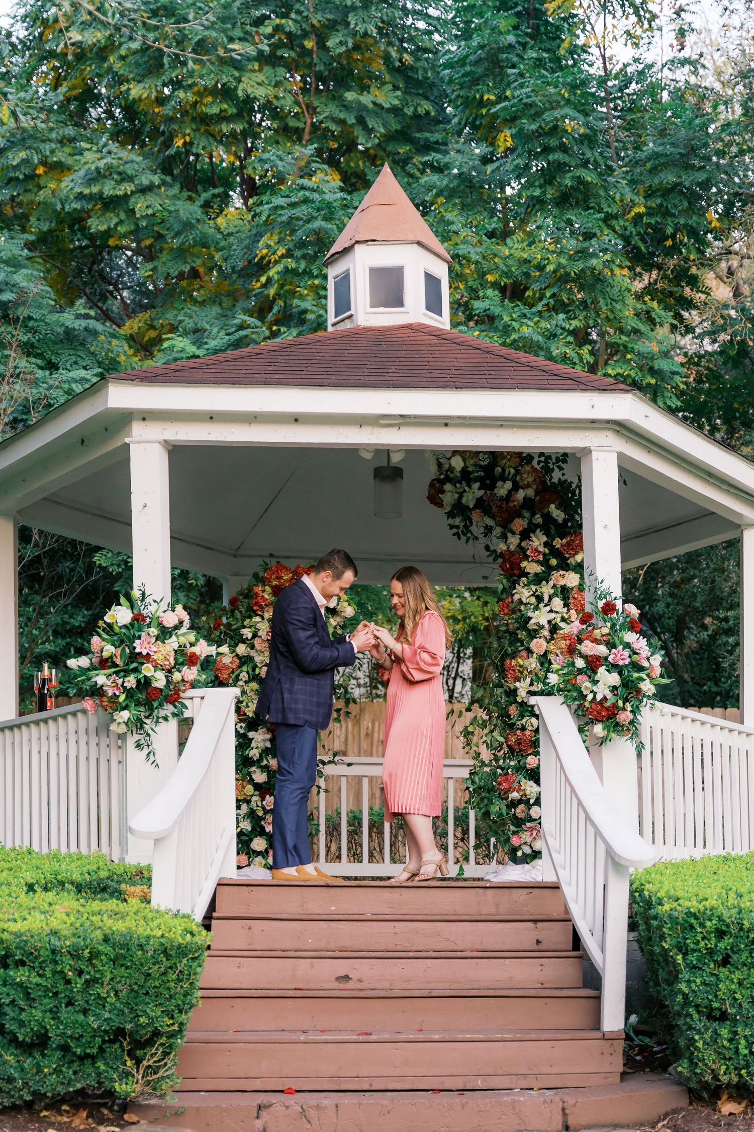A romantic scene unfolds on a garden gazebo decorated with fresh flowers and white columns.