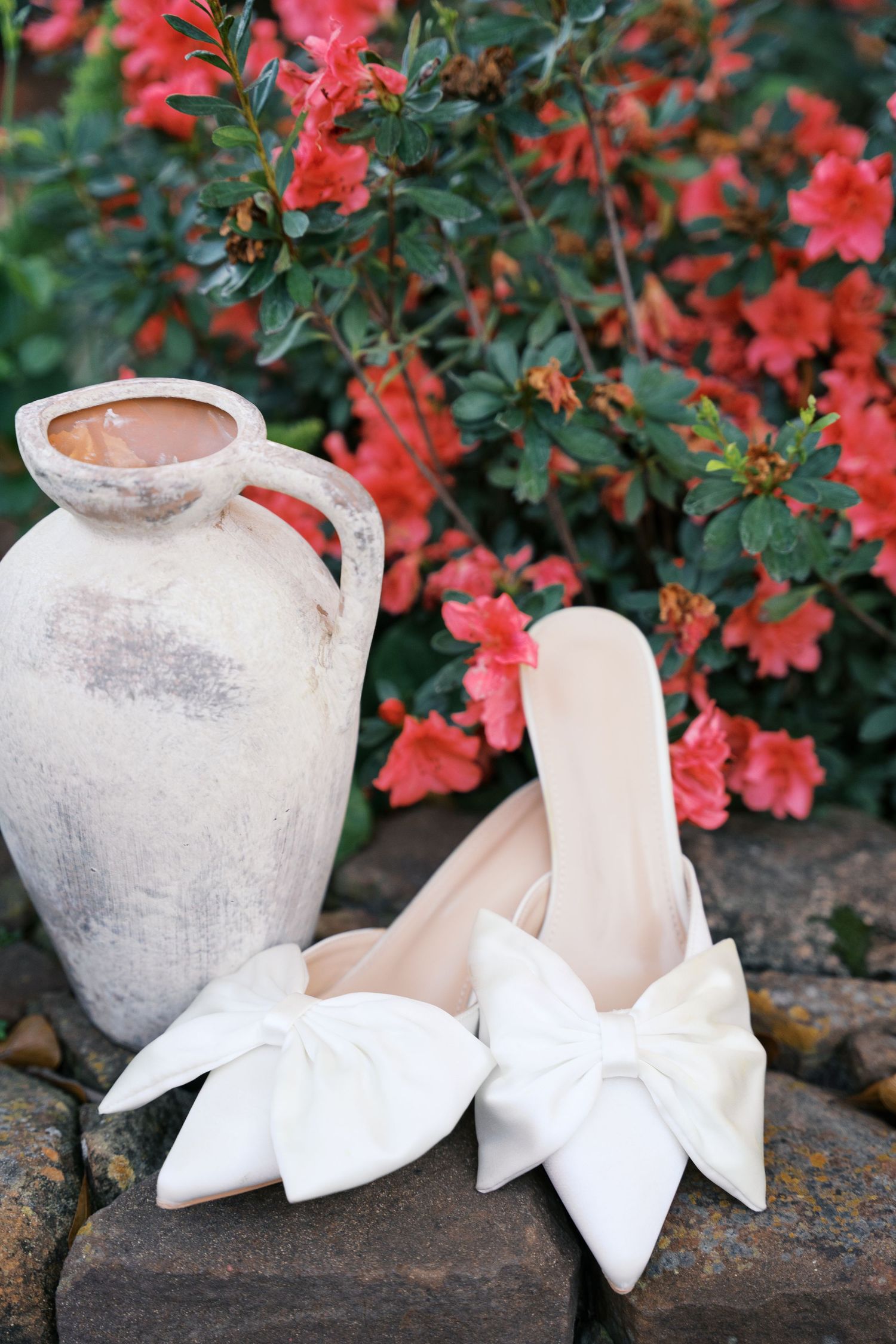 White bridal shoes arranged near coral flowers and a rustic pottery vase.