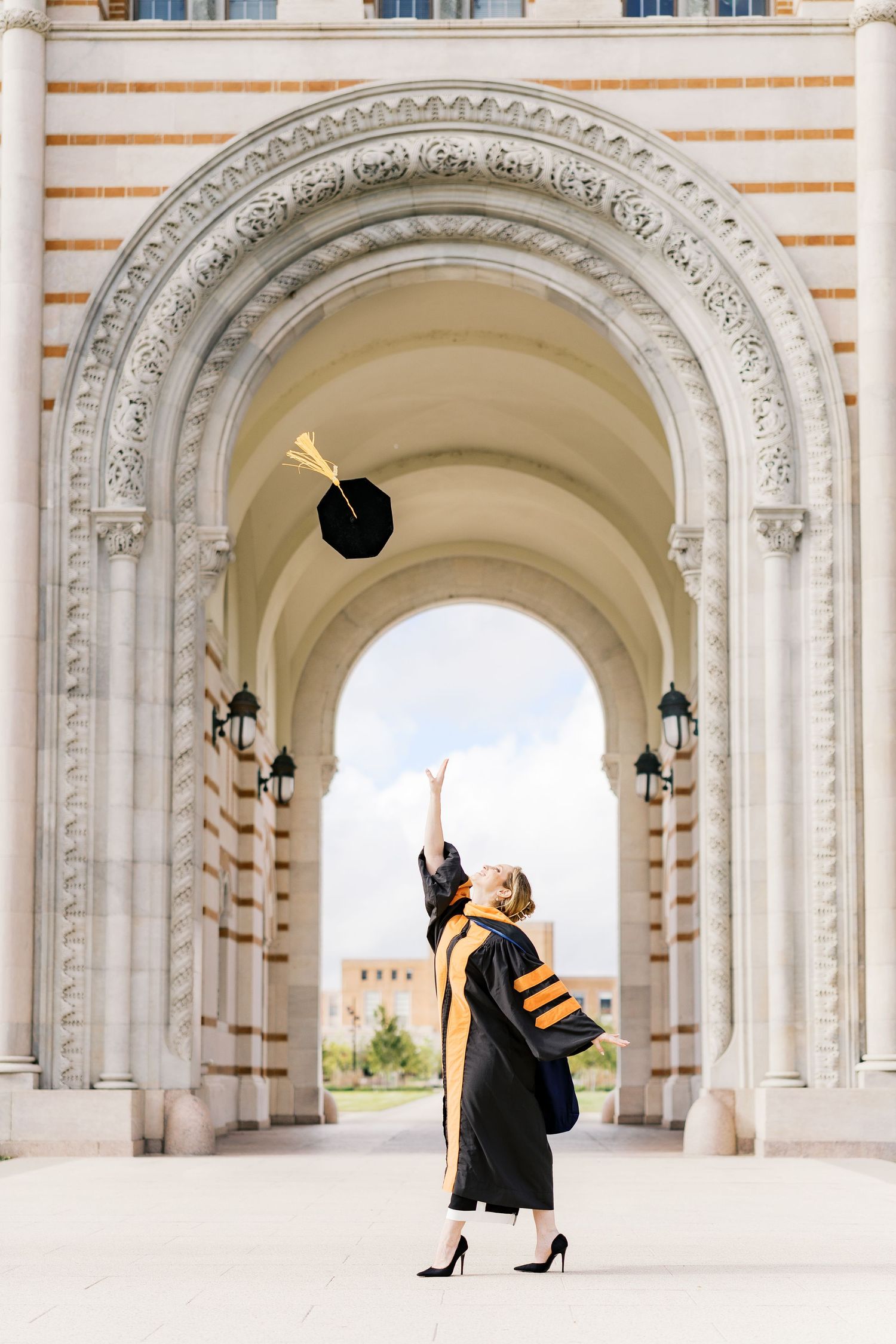 Graduation photoshoot under ornate white archways with cap toss celebration.