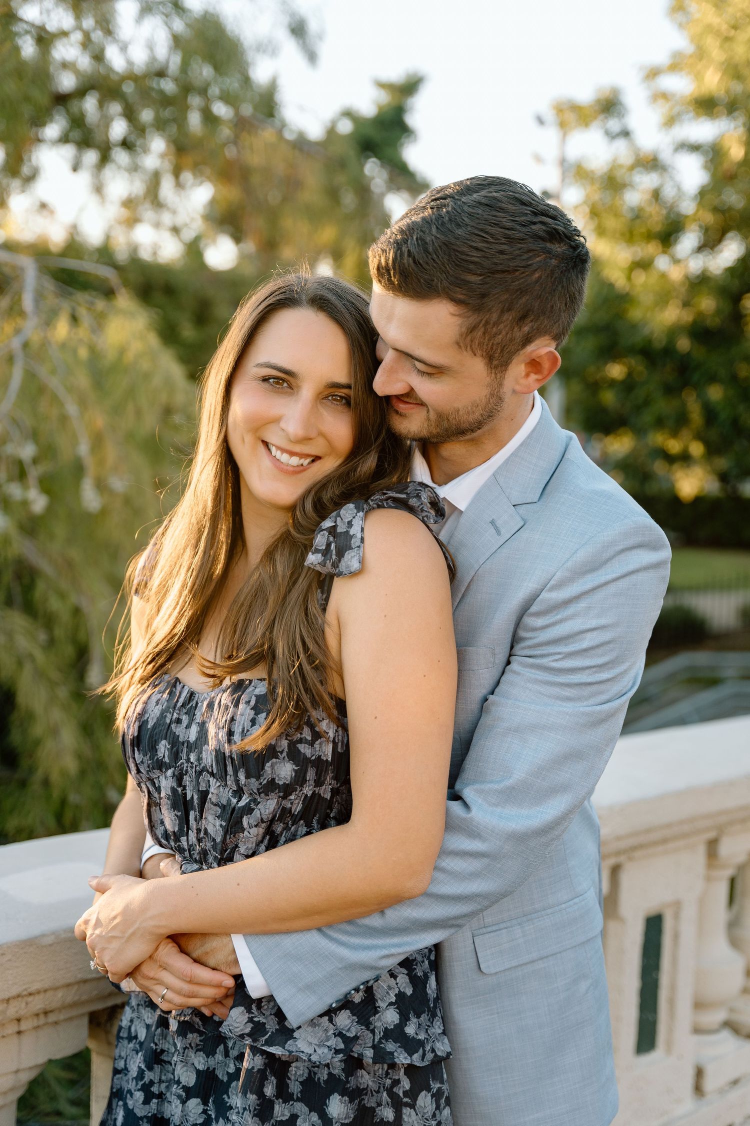 A couple embraces during sunset while wearing formal attire against a natural backdrop.