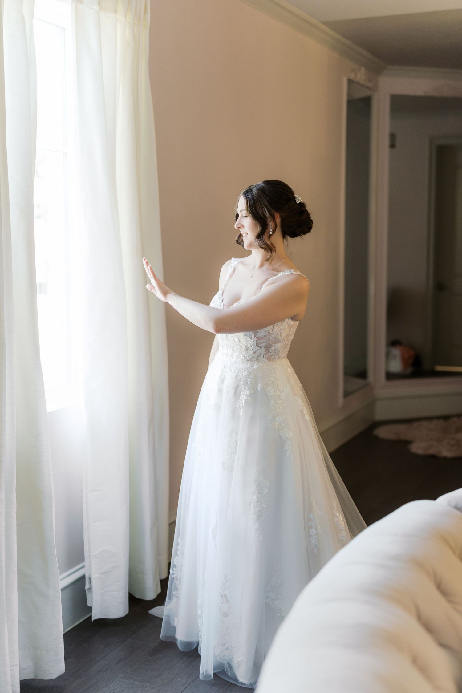 A bride in a flowing white dress twirls among sheer curtains in a bright room.