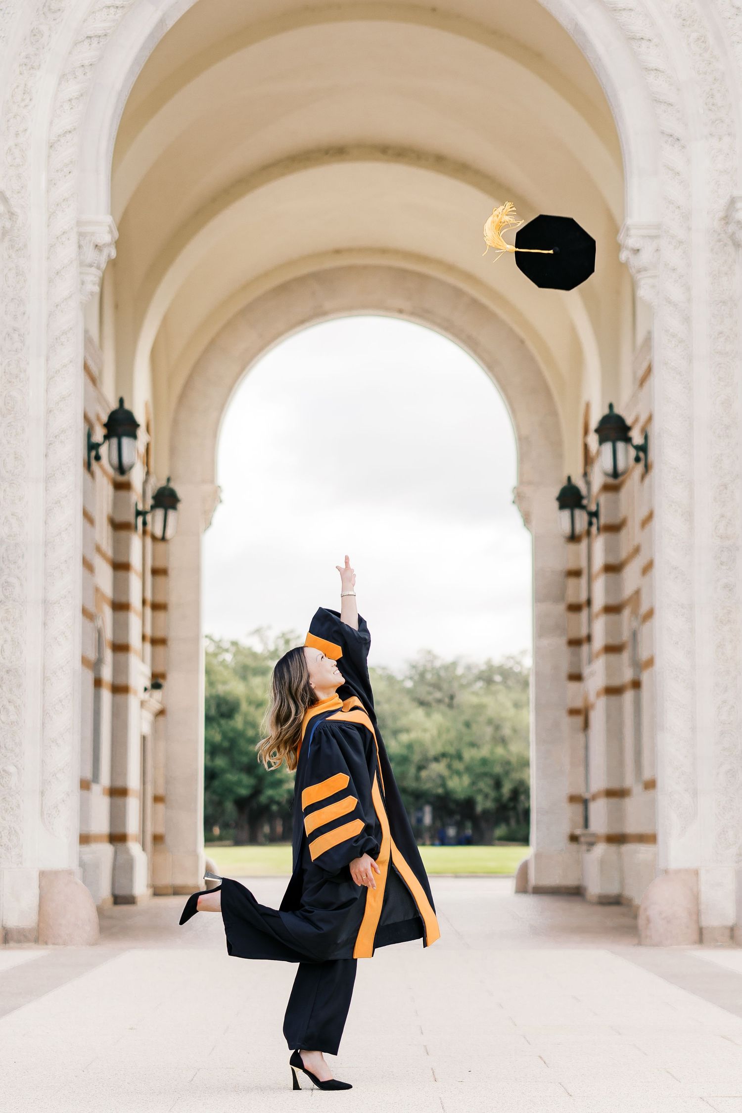 Graduate in academic regalia poses under ornate white archways of a classical building.