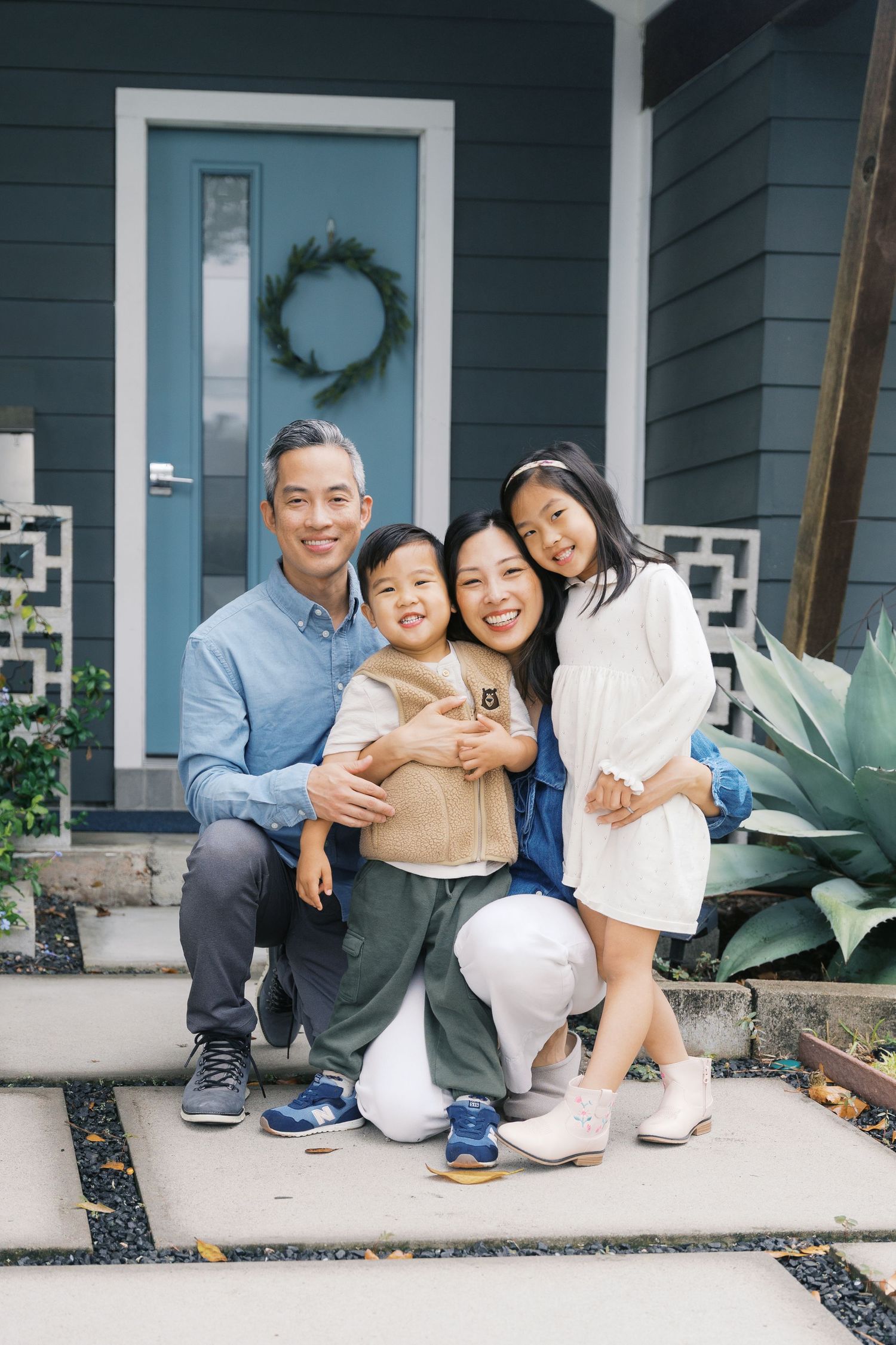 Family sitting on front porch steps of a navy blue house with white trim.