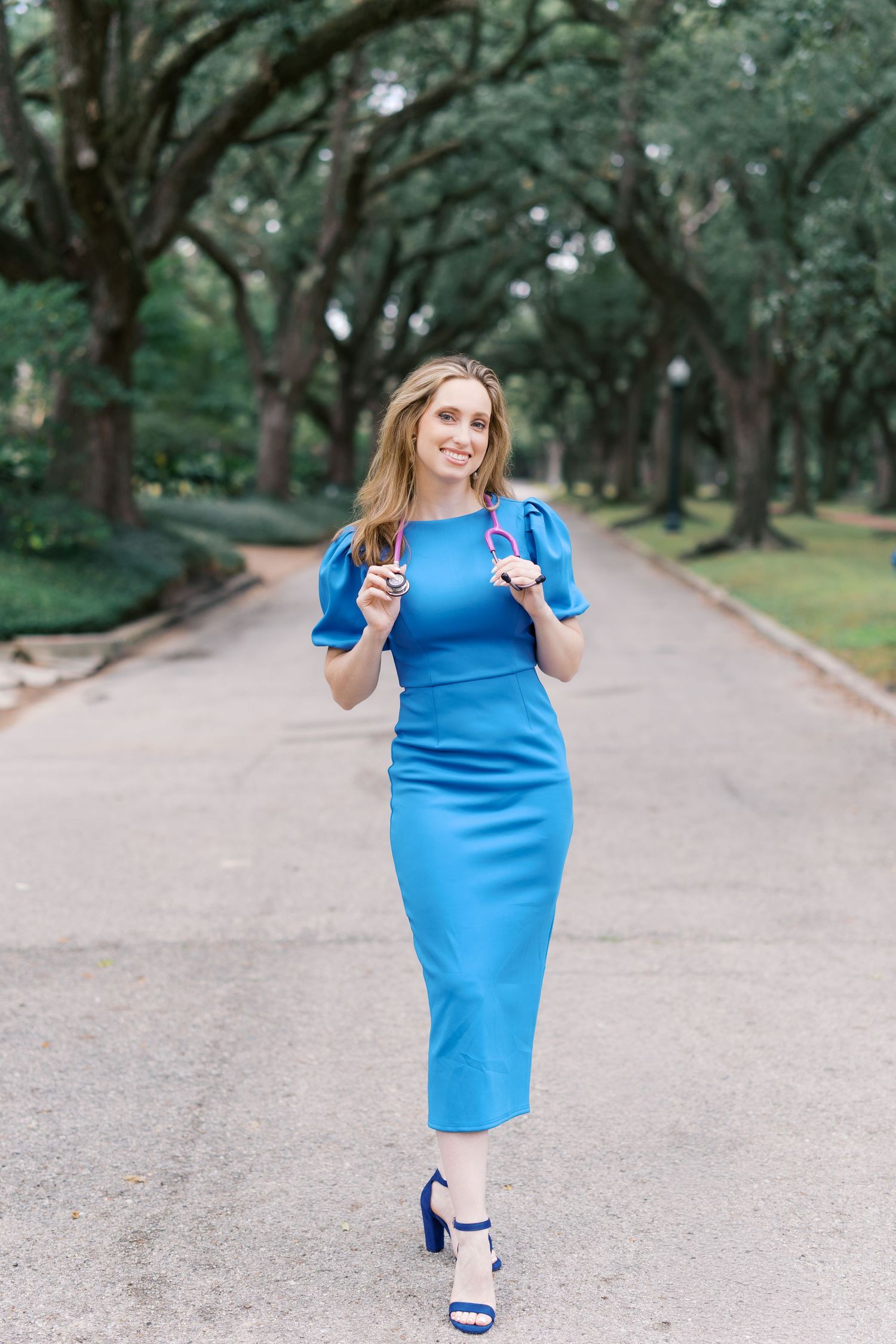 Maternity photoshoot featuring bright blue dress along scenic park pathway.
