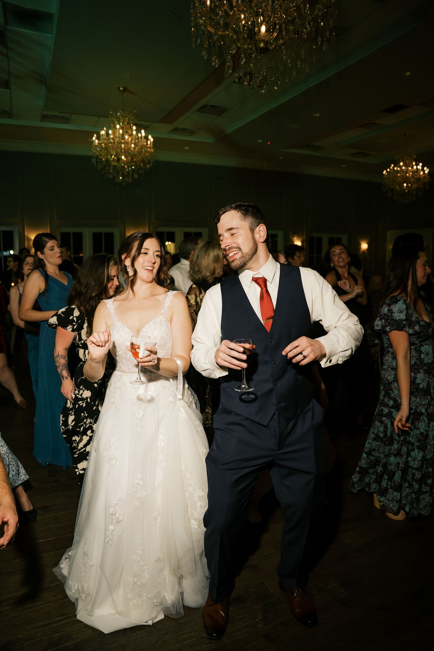 A couple shares a joyful dance moment at their wedding reception under sparkling chandeliers.