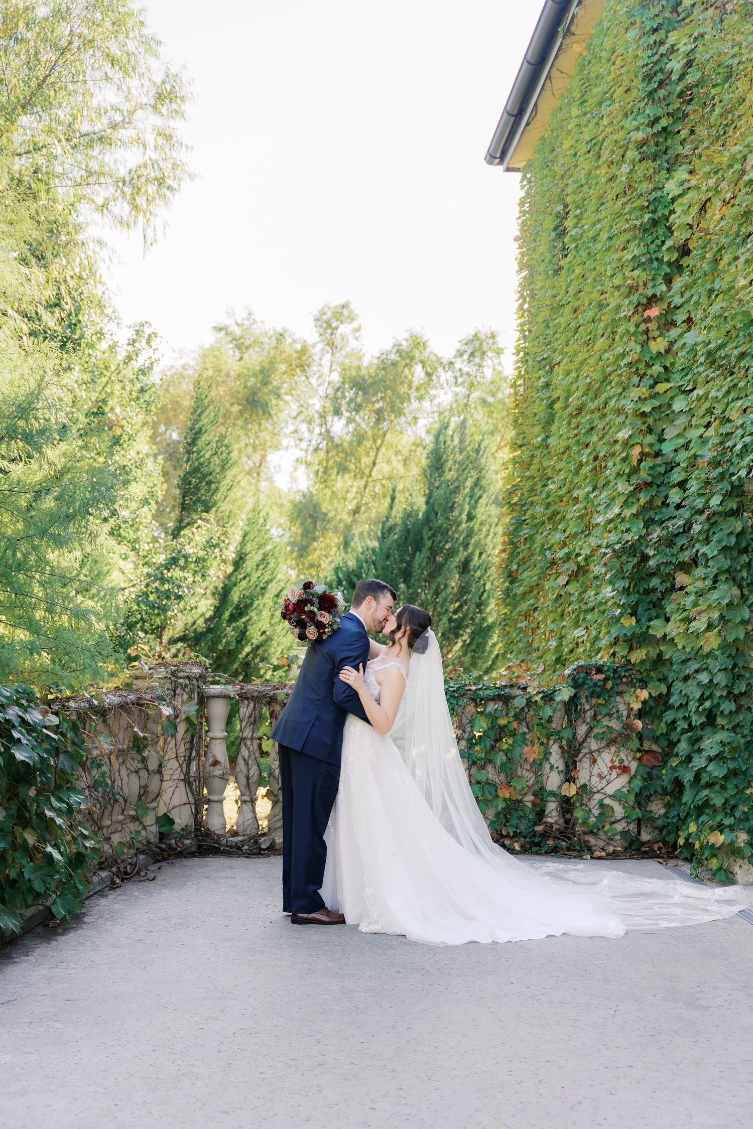 Wedding couple sharing an intimate moment in a garden setting with ivy-covered walls.