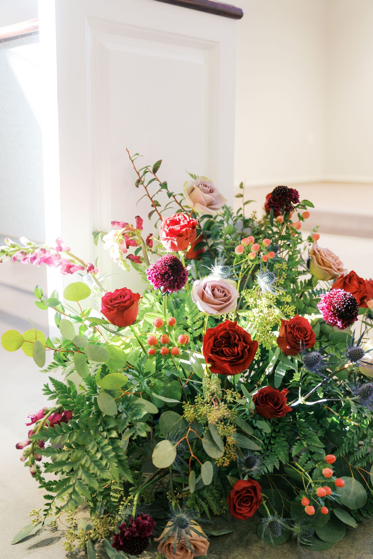Lush floral arrangement features deep red roses and mixed greenery.