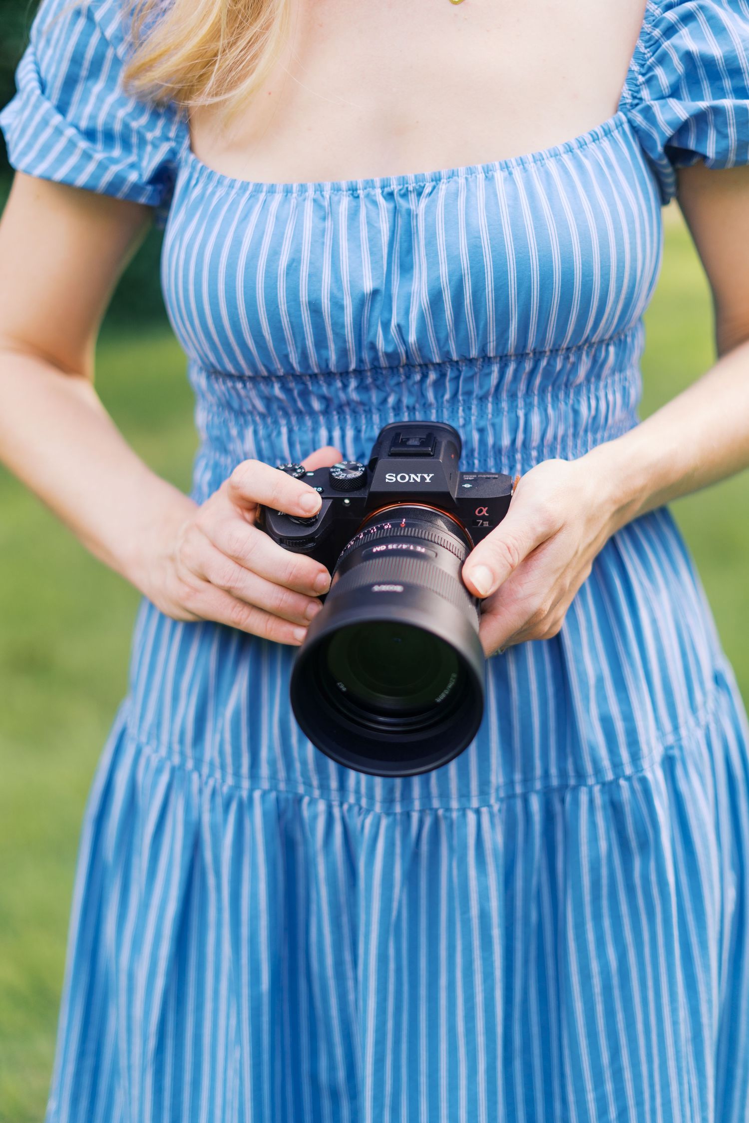 Woman in blue striped dress demonstrates using professional Sony camera.