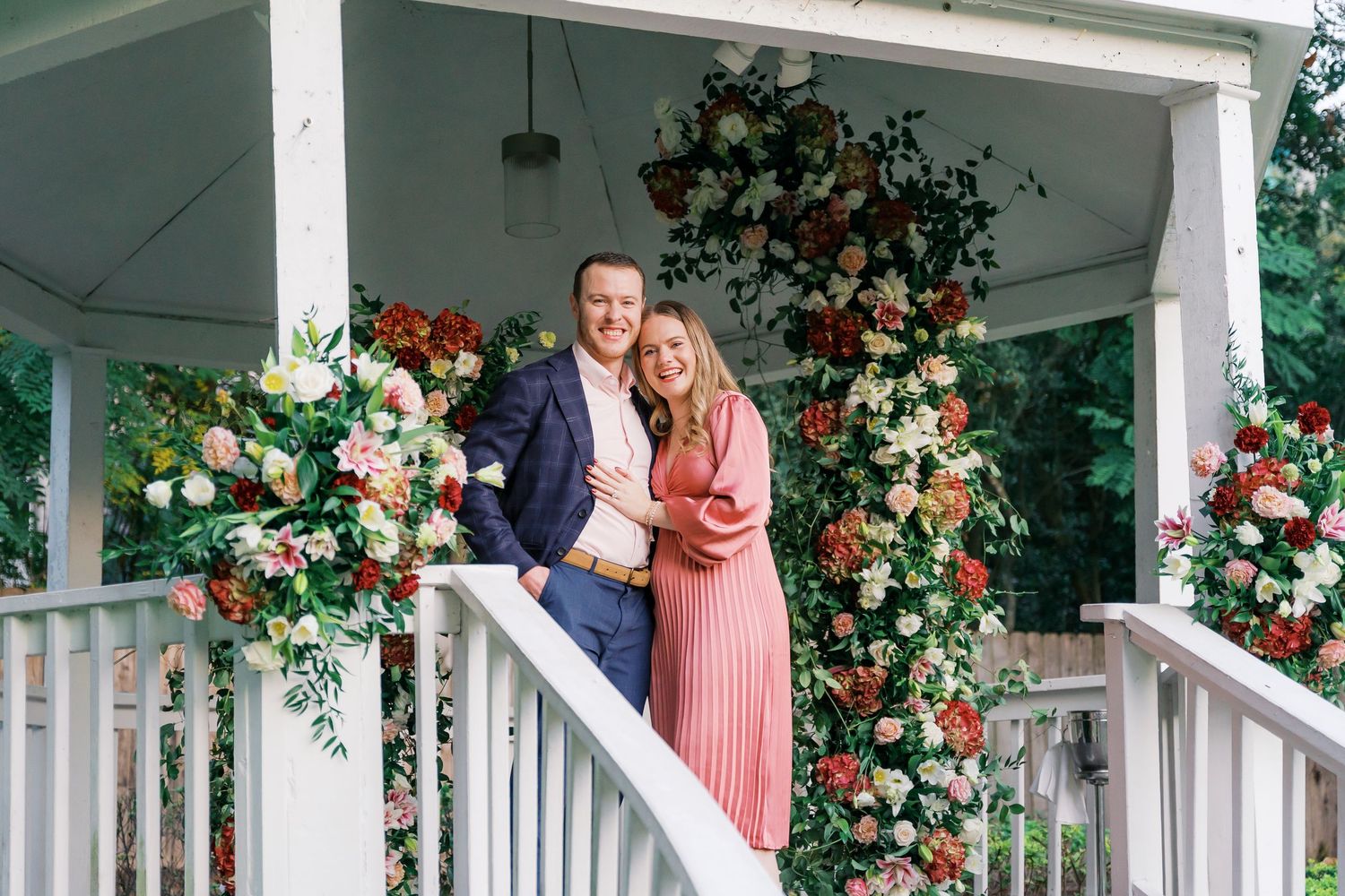 An intimate scene on a white-pillared gazebo deck adorned with pink and white floral arrangements.